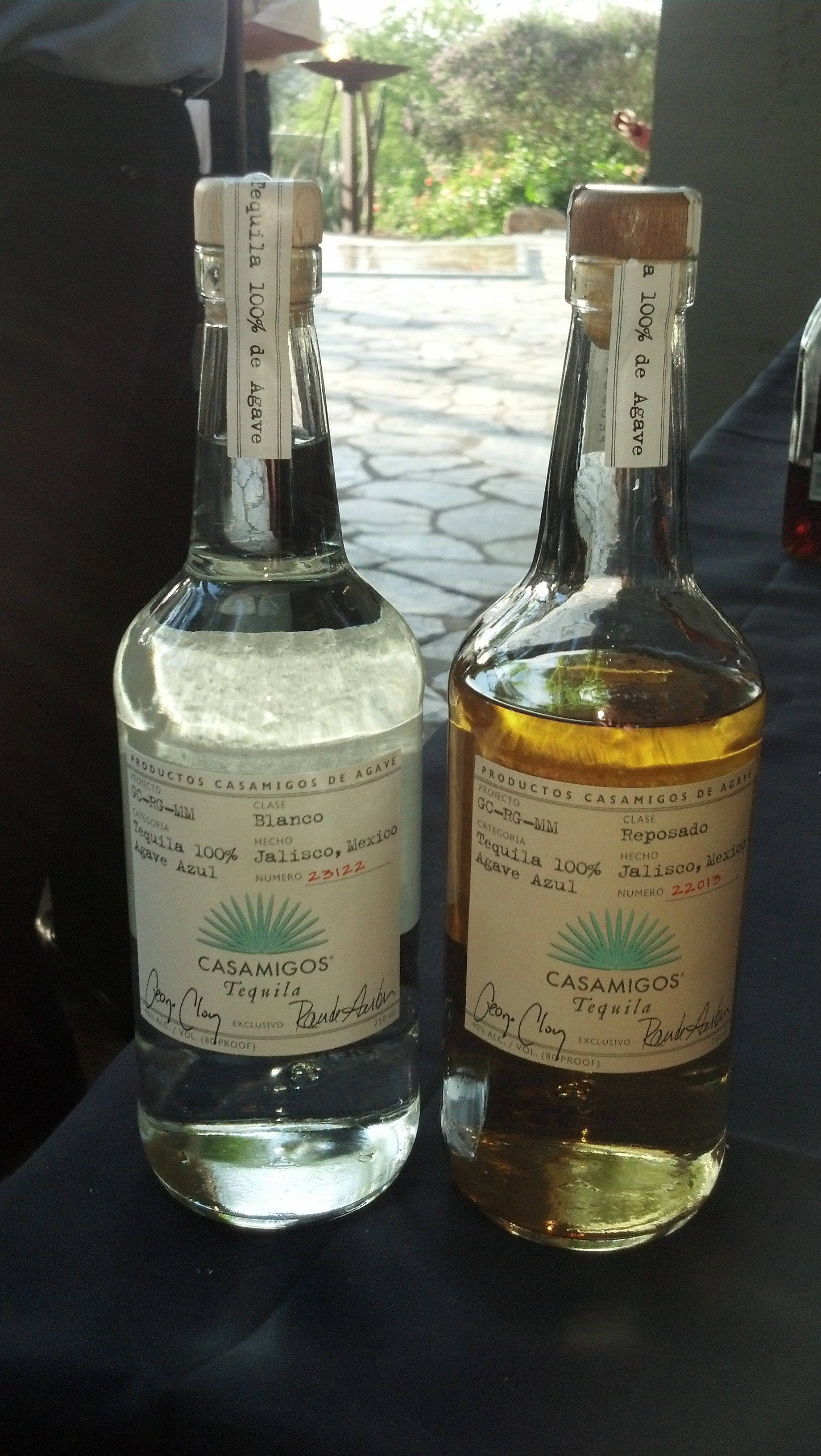 bottle 桌布 壁紙 — 兩瓶Casamigos龍舌蘭酒blanco和reposado並排放在一張深色桌子上，後面可見戶外綠植。
