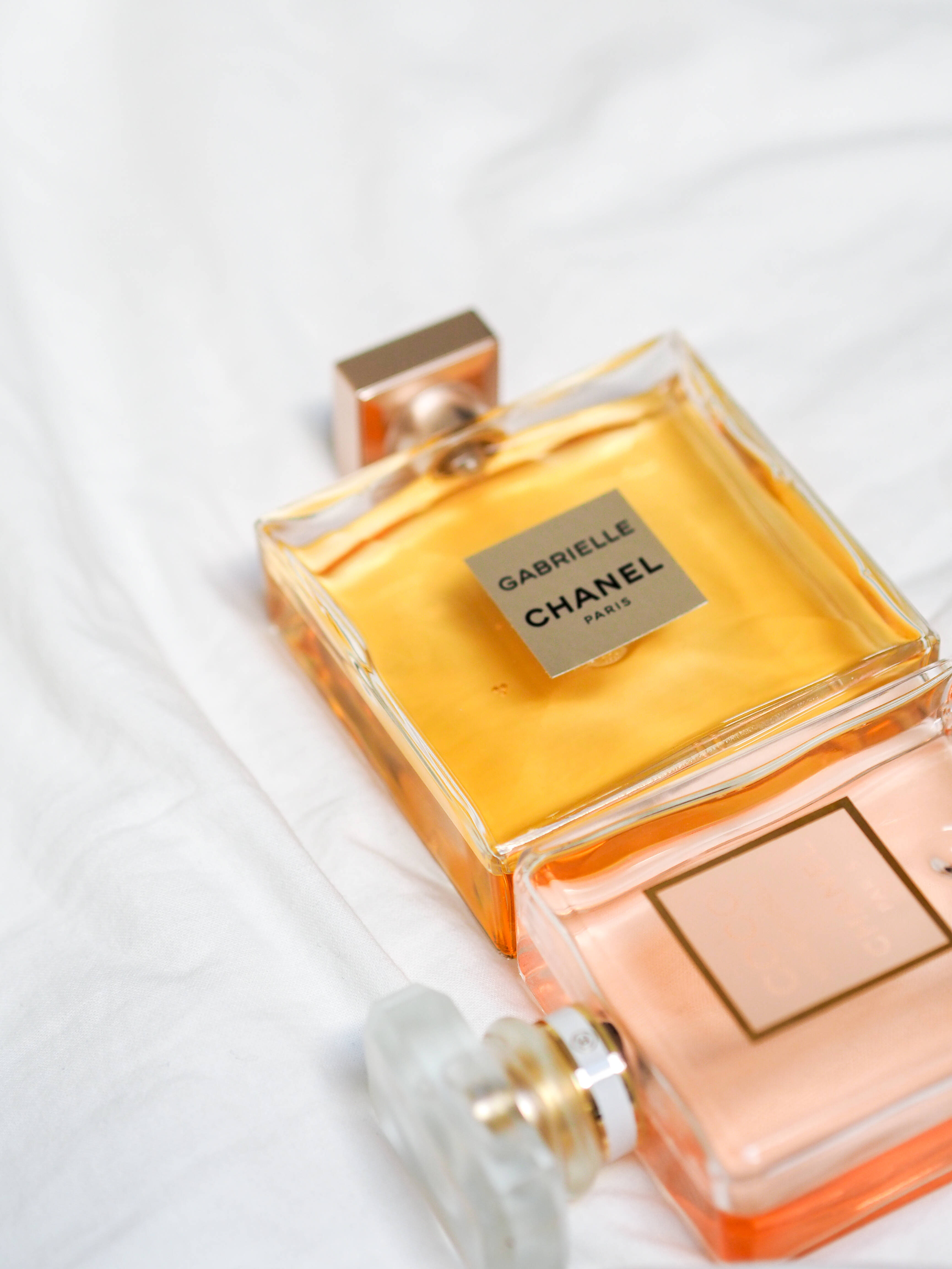 Pinterest 桌布 壁紙 — 兩瓶Chanel Gabrielle香水瓶的特寫，金色和桃色液體放在白色布料上。