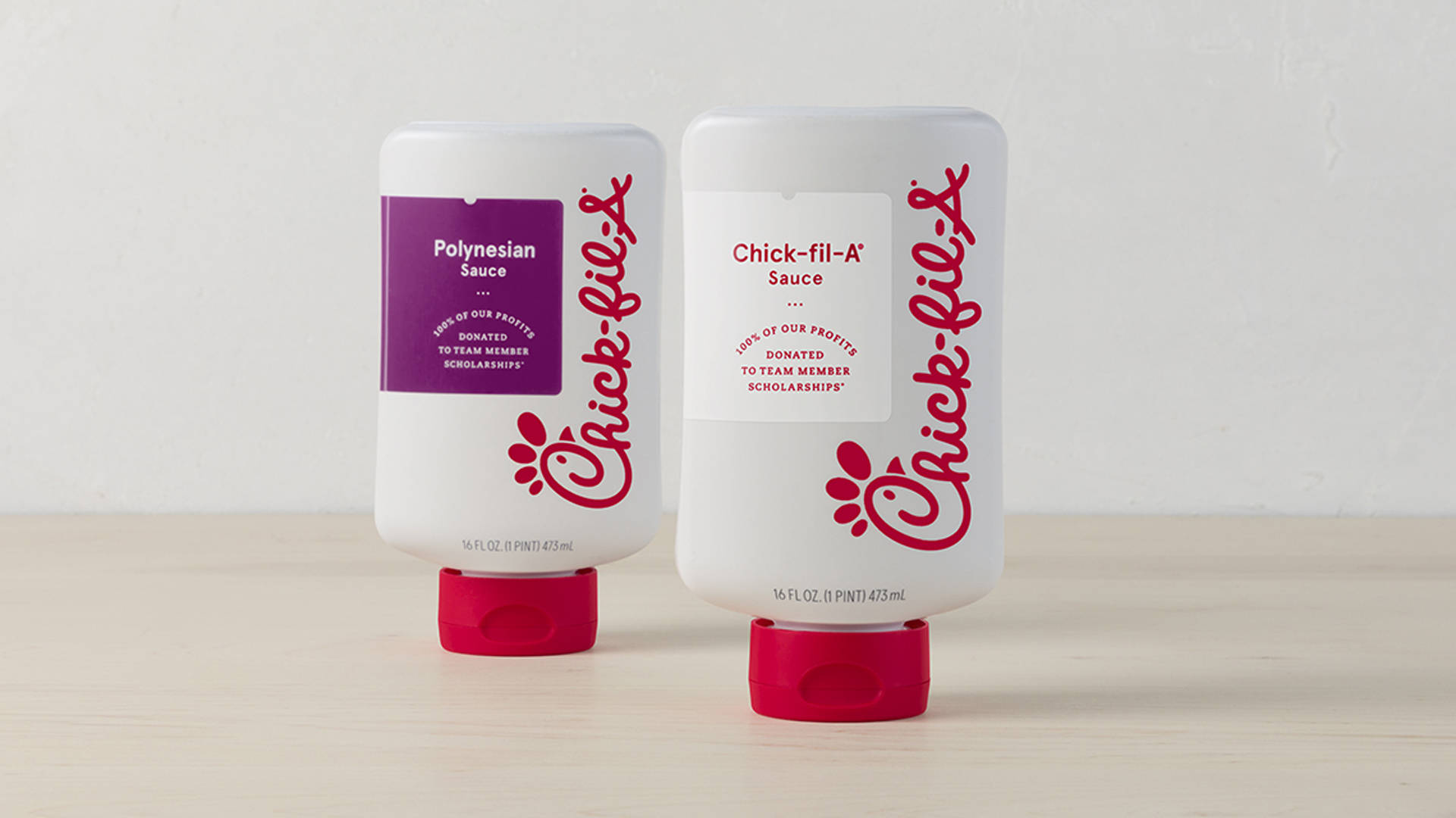 chick 桌布 壁紙 — 兩瓶Chick-fil-A醬料瓶，一瓶波利尼西亞風味一瓶原味，並排放在淺色木質表面上，背景是純白牆壁。