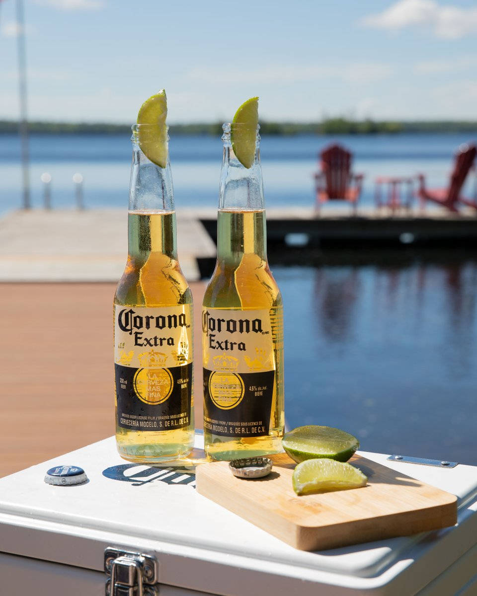 corona 桌布 壁紙 — 兩瓶Corona Extra啤酒搭配萊姆角，放在湖邊碼頭的冷卻器上，天空湛藍明亮。