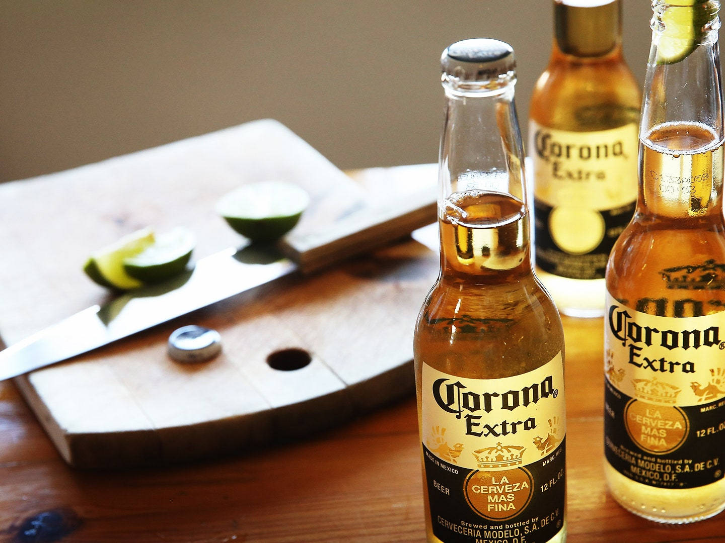 corona 桌布 壁紙 — 兩瓶Corona Extra啤酒連萊姆角放在木桌上，旁邊有砧板、刀和半個萊姆。
