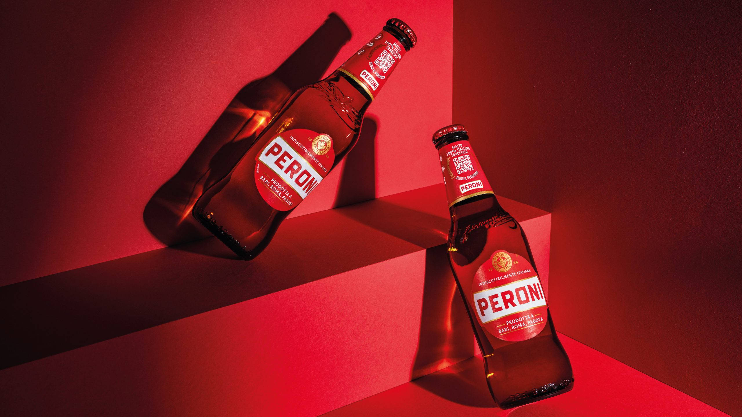 Beer 桌布 壁紙 — 兩瓶Peroni啤酒在攝影棚燈光下，於鮮紅色幾何造型佈景上投射出戲劇性的陰影。
