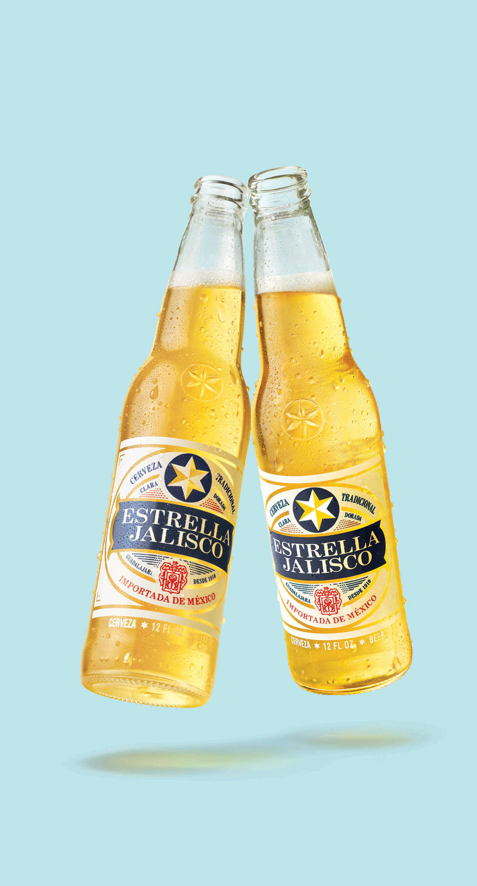 alcohol 桌布 壁紙 — 兩瓶冰涼的Estrella Jalisco啤酒在柔和的藍色背景前碰撞，可見冷凝水滴。