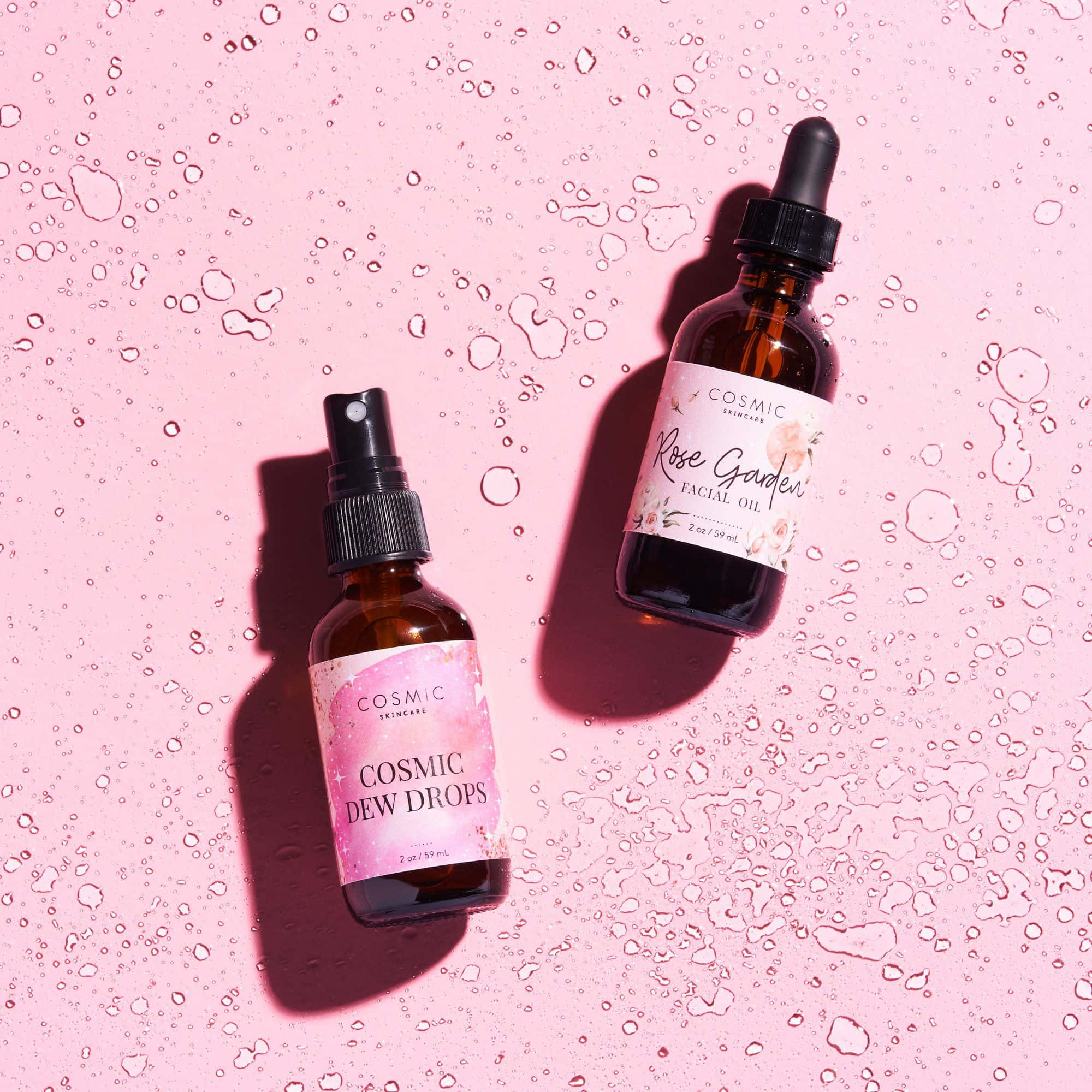 Rose Oil 桌布 壁紙 — 兩瓶琥珀色護膚品，標籤為 Cosmic Dew Drops 和 Rose Garden Facial Oil，放在一個佈滿水滴的粉紅色表面上，處於明亮光線下。