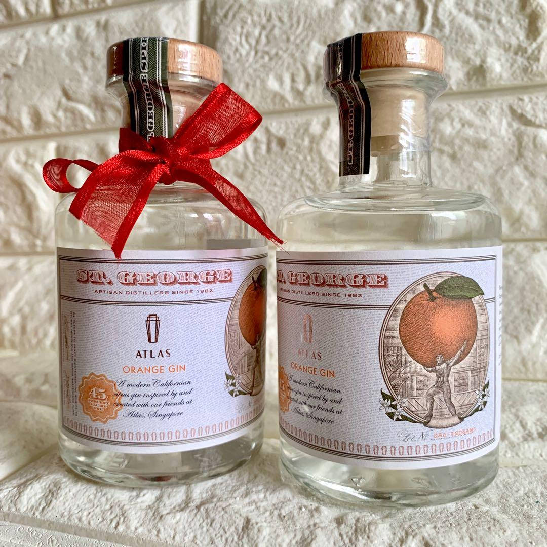 bottle 桌布 壁紙 — 兩瓶透明玻璃的 St George Atlas Orange Gin 並排放置在紋理石面上，其中一瓶飾有紅色絲帶。