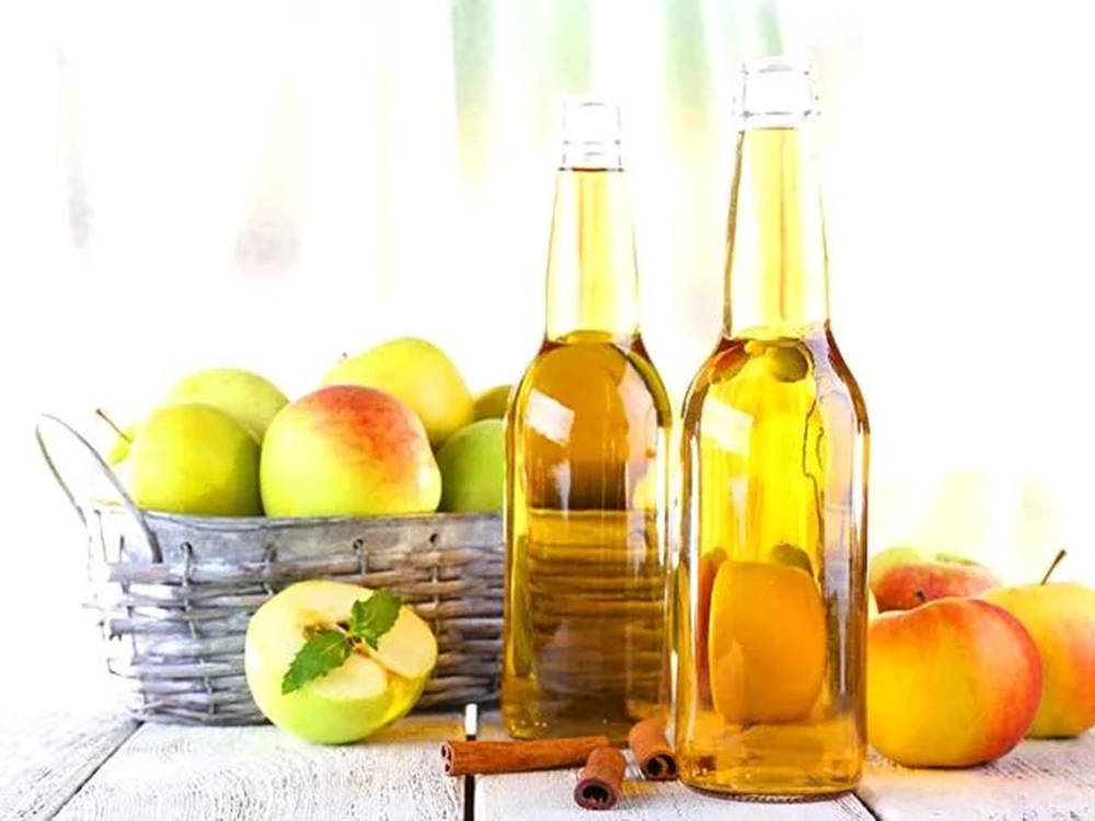 Drink 桌布 壁紙 — 兩瓶金色蘋果酒玻璃瓶放在白色木桌上，旁邊有一籃新鮮的青蘋果和紅蘋果。