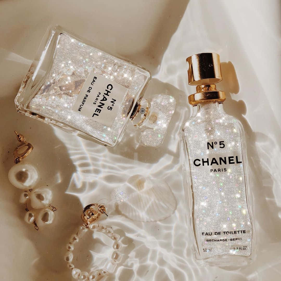 Boujee Aesthetic 桌布 壁紙 — 兩瓶閃閃發光的Chanel No5香水瓶和珍珠首飾放在陽光照射的白色布料上，帶有柔和陰影。