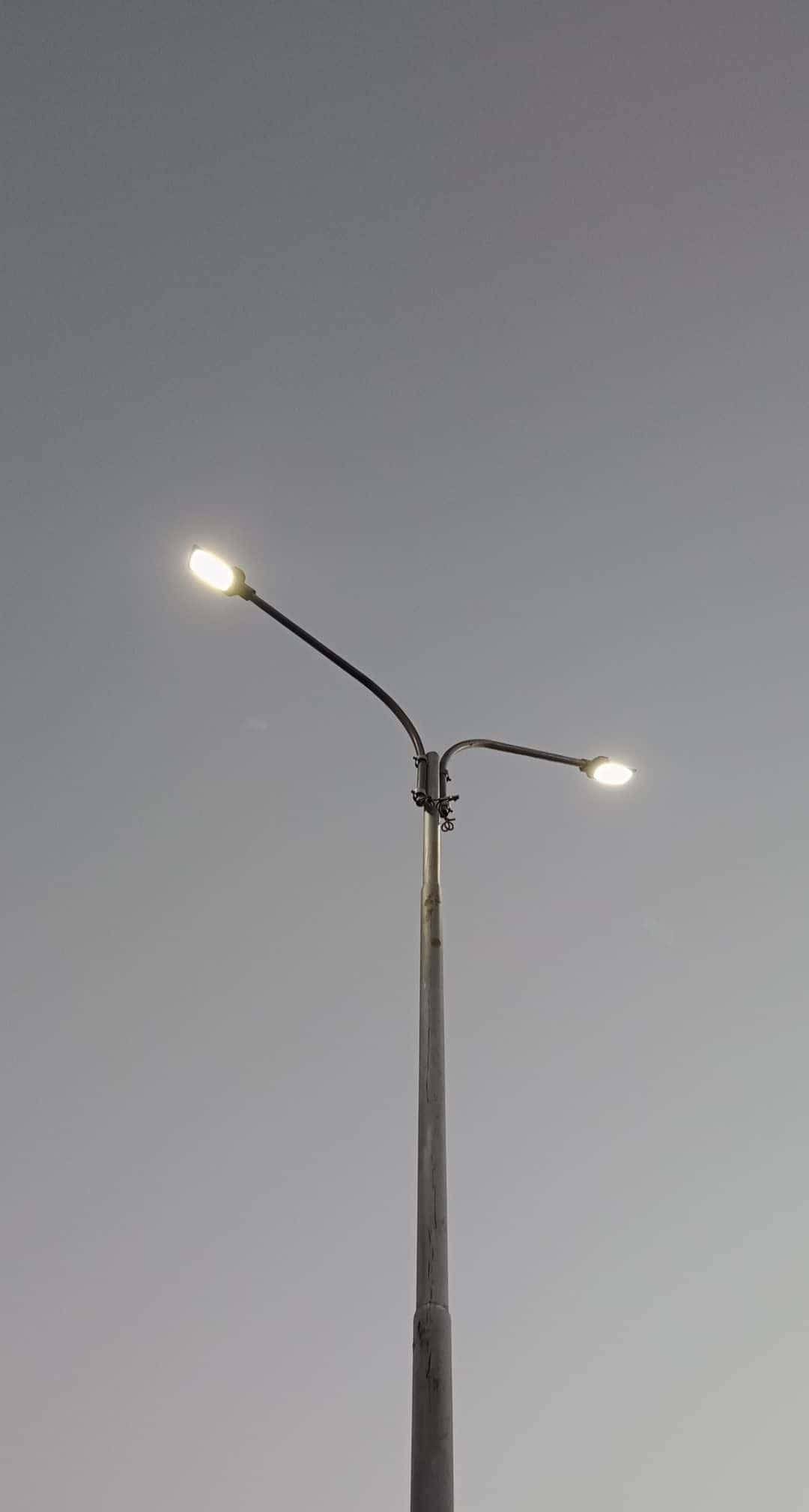 Minimalist Photography 桌布 壁紙 — 兩盞發光的街燈從一根高桿上延伸出來，映襯著柔和的暮色天空。