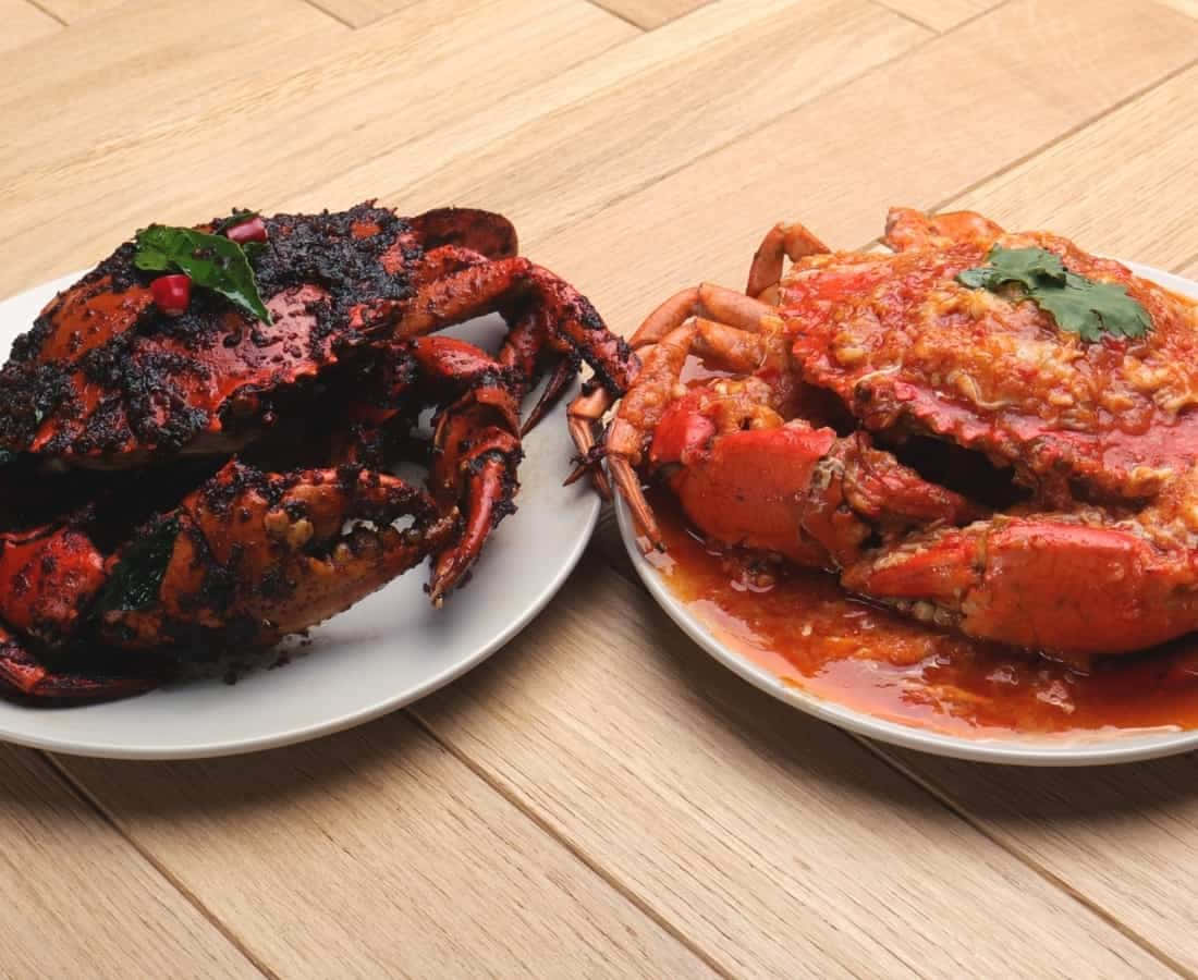 Food Photography 桌布 壁紙 — 兩盤充滿活力的香料蟹，一盤燒焦黑色，另一盤在濃郁的紅色醬汁中，用香草裝飾，放在木桌上。
