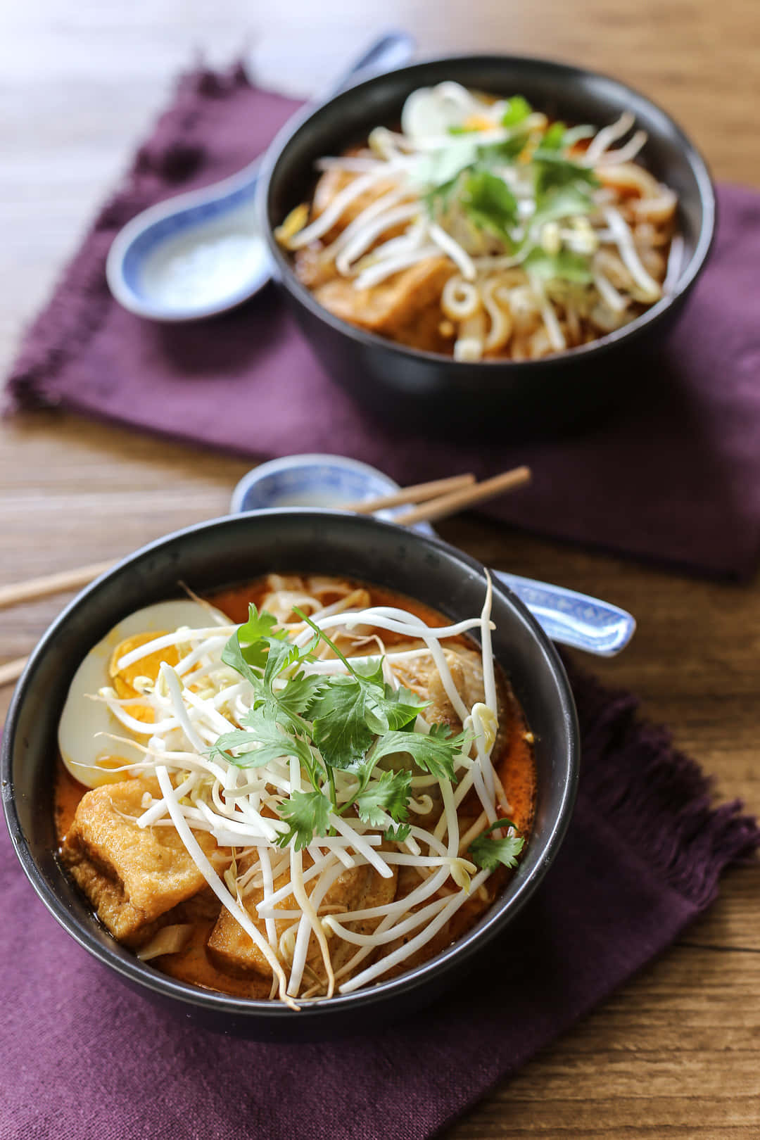 Delicious Food 桌布 壁紙 — 兩碗冒著熱氣的湯麵，上面放著豆芽、香菜和豆腐，放在一張鋪有紫色餐巾的木桌上。