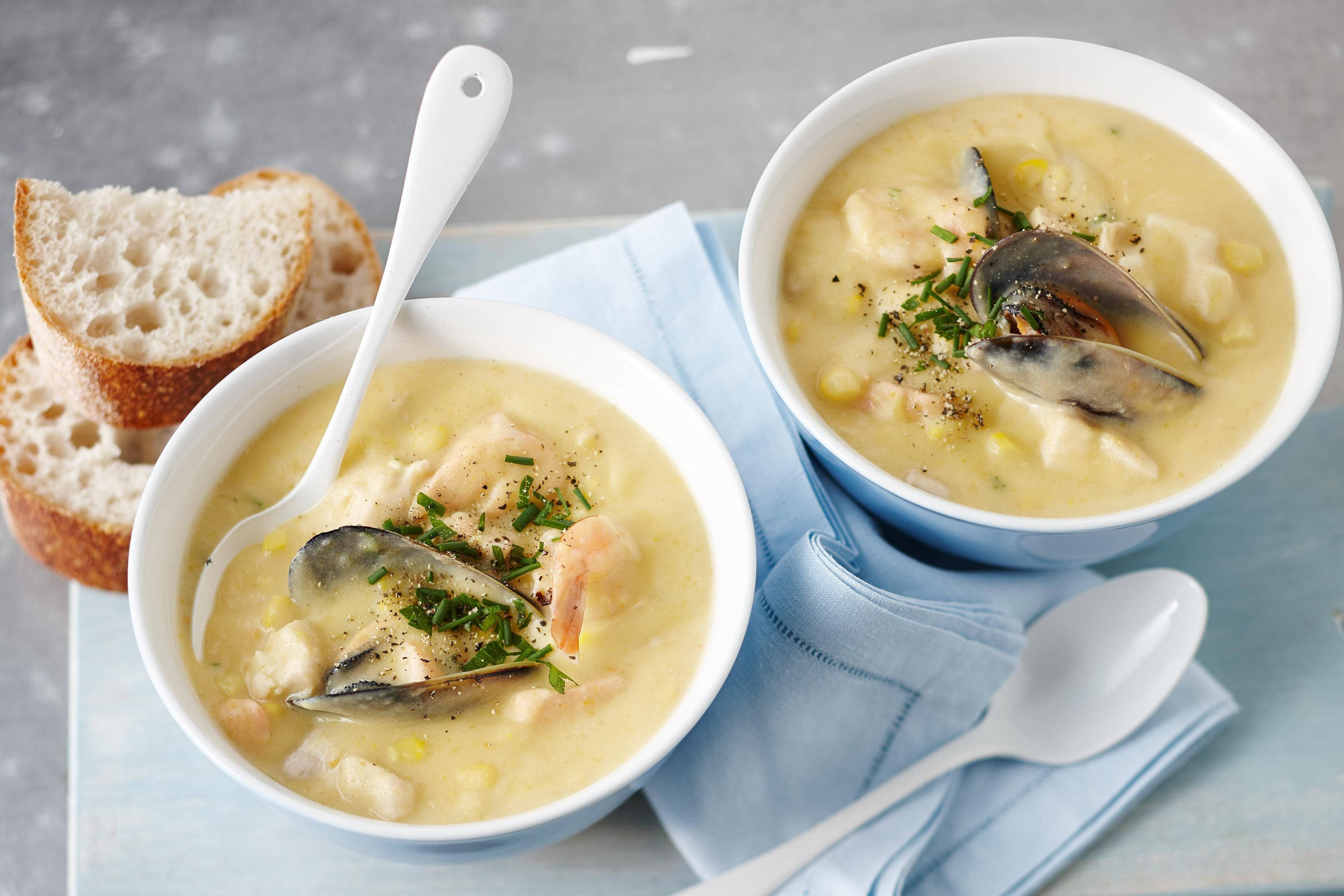 Chowder 桌布 壁紙 — 兩碗奶油海鮮濃湯，配有淡菜、蝦和玉米，以香草和脆皮麵包裝飾，放在藍色餐巾上。