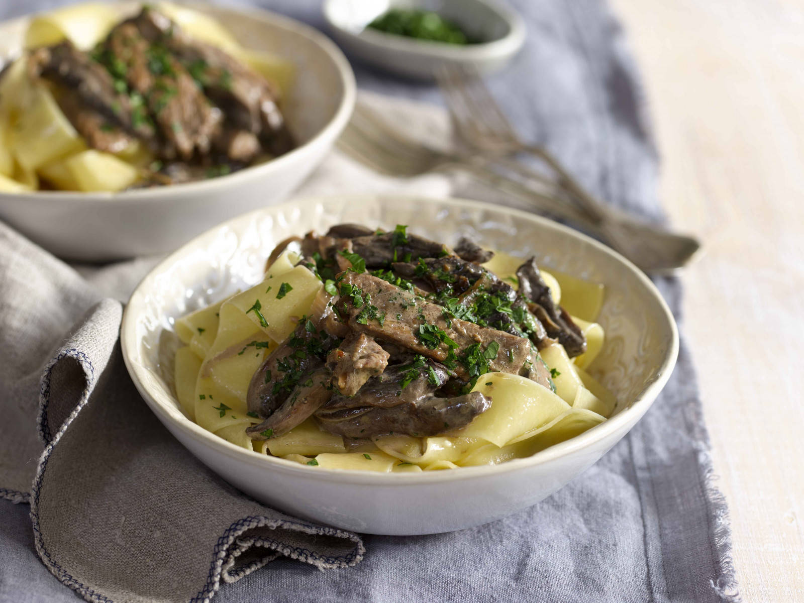 Pasta 桌布 壁紙 — 兩碗奶油牛肉斯特羅加諾夫配寬麵條，飾以新鮮歐芹，放在有紋理的灰色布上。
