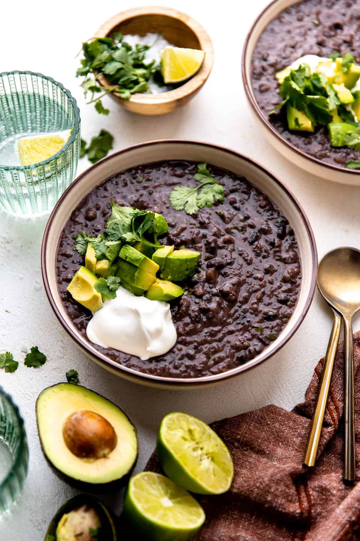 Black Bean Soup 桌布 壁紙 — 兩碗濃郁黑豆，上面鋪上酪梨、香菜和酸奶油，放在明亮的白色表面上。