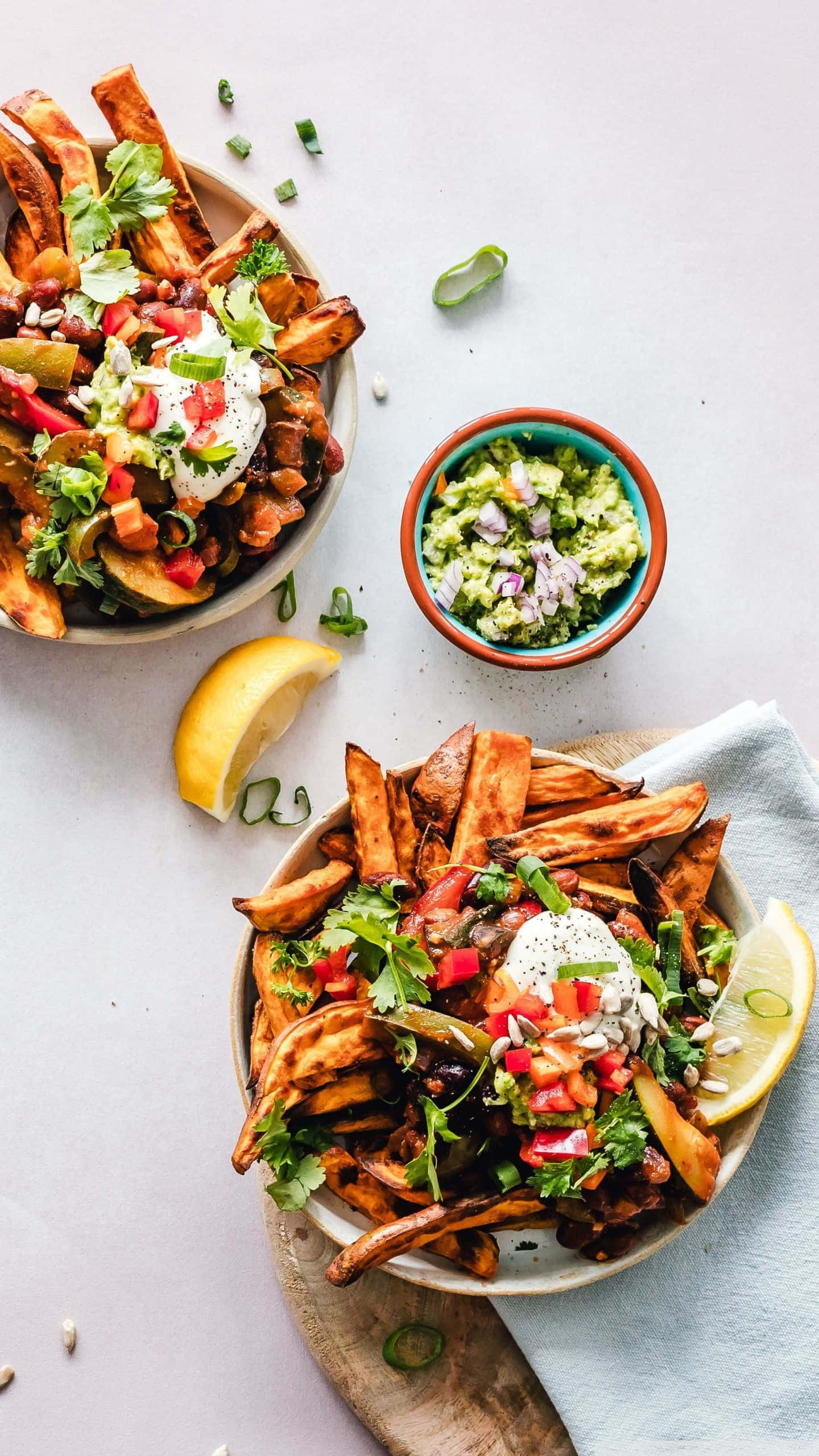 Fries 桌布 壁紙 — 兩碗色彩繽紛的地瓜條，上面放有酪梨醬、酸奶油和新鮮蔬菜，置於淺色表面上。