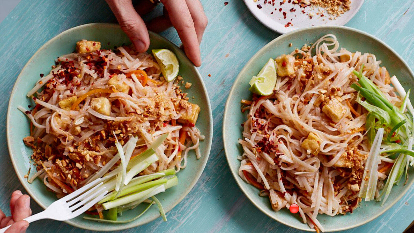 thai 桌布 壁紙 — 兩碗色彩繽紛的泰式炒金邊粉，配上花生、萊姆和蔬菜，放在藍綠色木桌上。