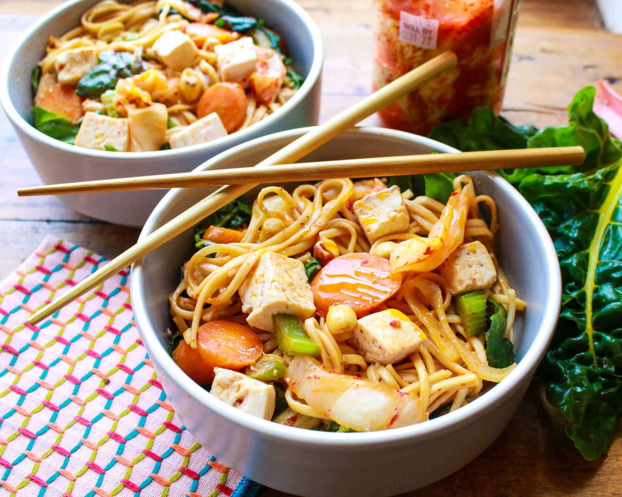 Noodles 桌布 壁紙 — 兩碗色彩繽紛的炒麵，配有豆腐、蝦、胡蘿蔔和青菜，放在彩色編織墊上，筷子擱在上面。