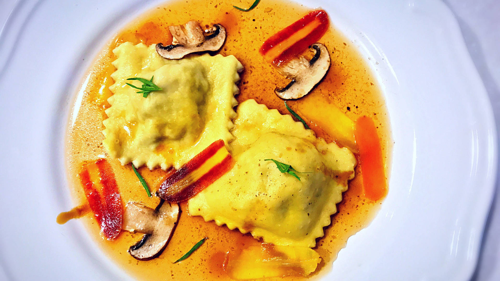 Pasta 桌布 壁紙 — 兩粒金黃色義大利餃浸在濃郁醬汁中，搭配烤紅椒和蘑菇，並以新鮮香草點綴。