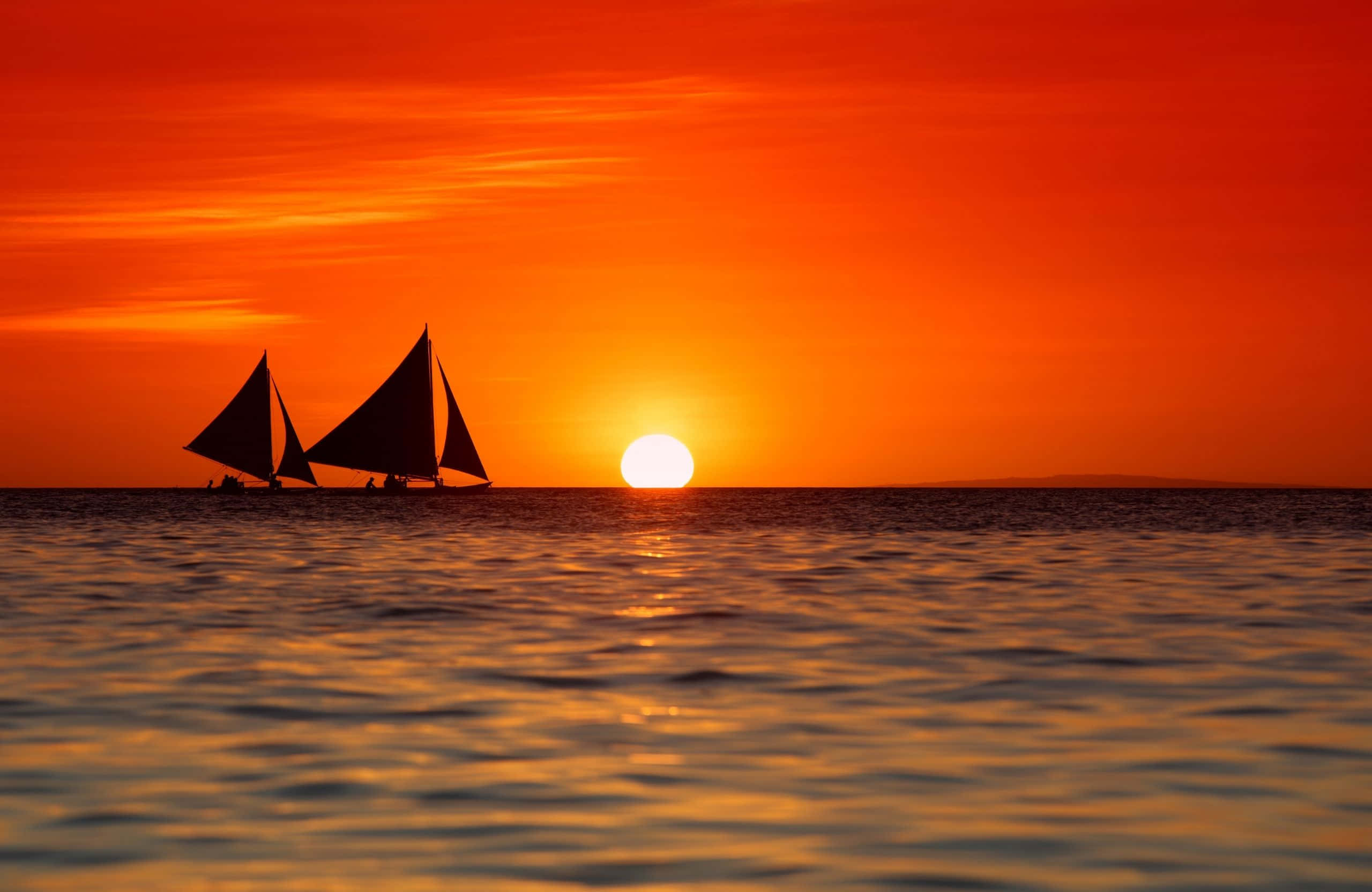 2560x1664 桌布 壁紙 — 兩艘帆船在平靜的水面上滑行，夕陽以火熱的橙色和紅色色調落下。