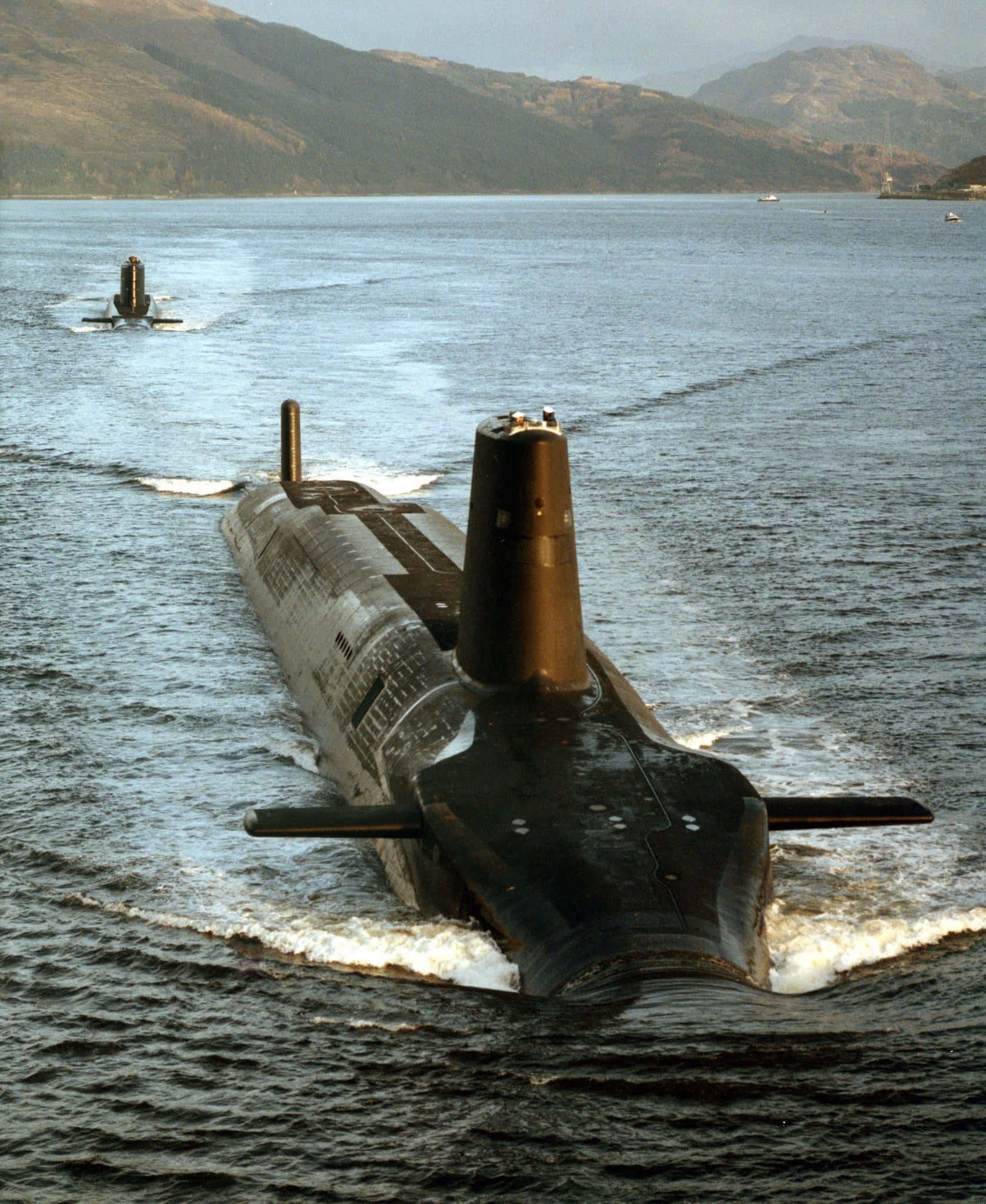 Submarine 桌布 壁紙 — 兩艘流線型的黑色潛艇在平靜的水域中滑行，遠處朦朧的山巒聳立。