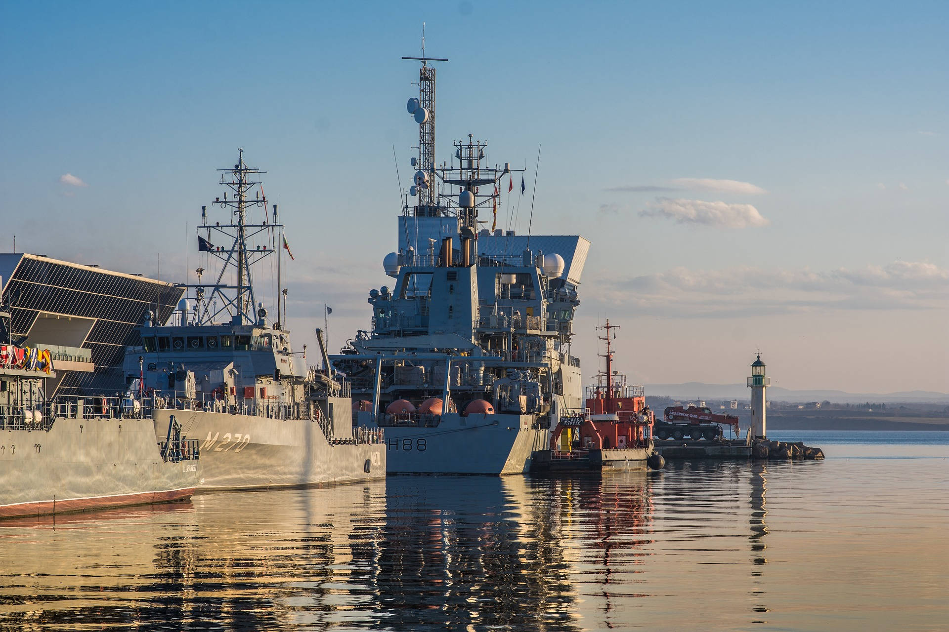 u s navy 桌布 壁紙 — 兩艘灰色軍艦停泊在平靜的水面上，在晴朗的藍天和遠山映襯下反射出金色的陽光。