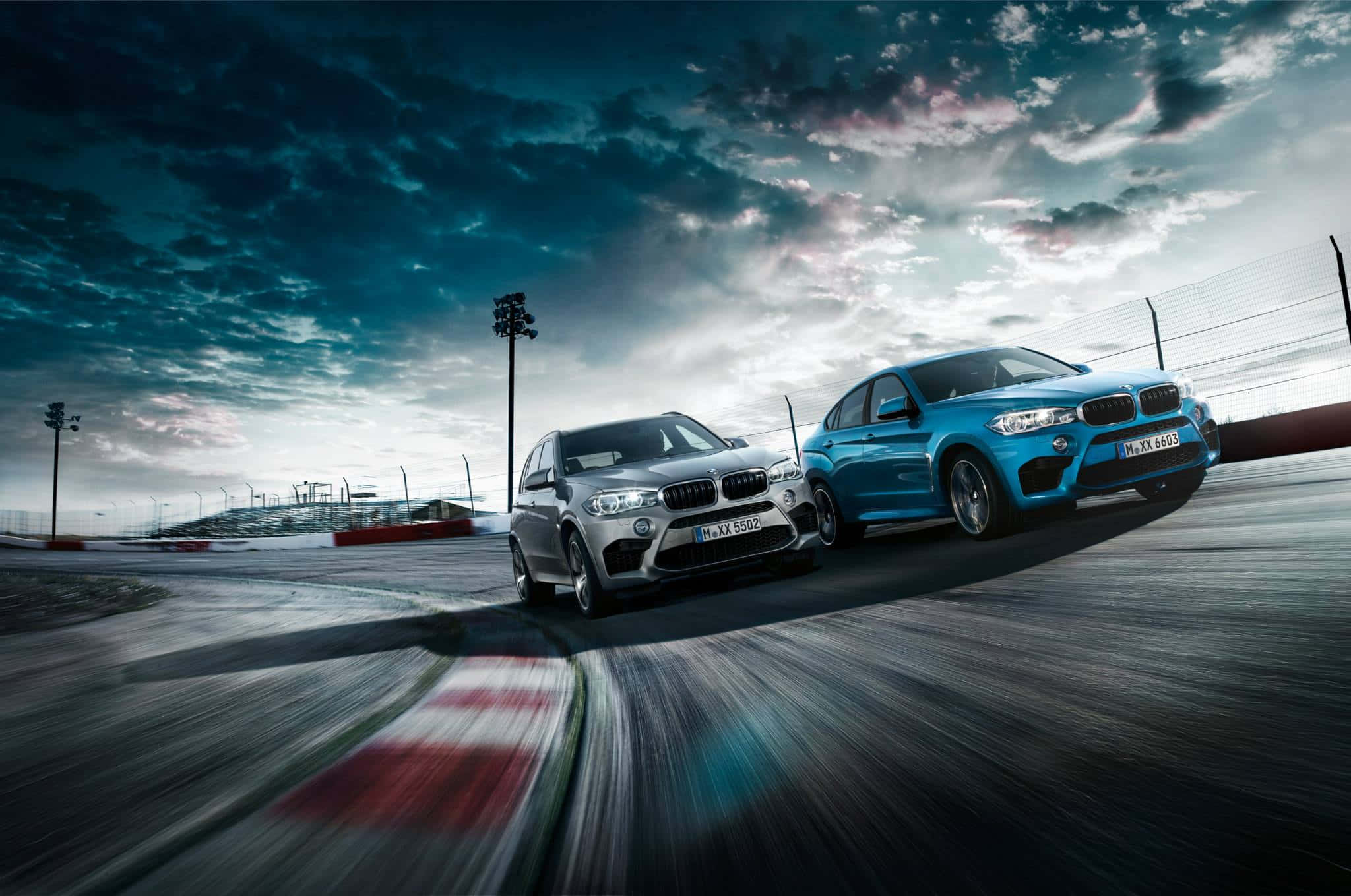Bmw X6 M 桌布 壁紙 — 兩輛BMW SUV在戲劇性的多雲天空下並排競速，帶有動態模糊效果。