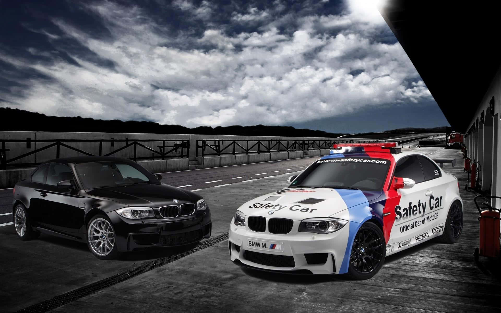 Safety Car 桌布 壁紙 — 兩輛BMW賽車，一黑一白，安全車帶有紅藍條紋，停在賽道上，天空風暴戲劇性。