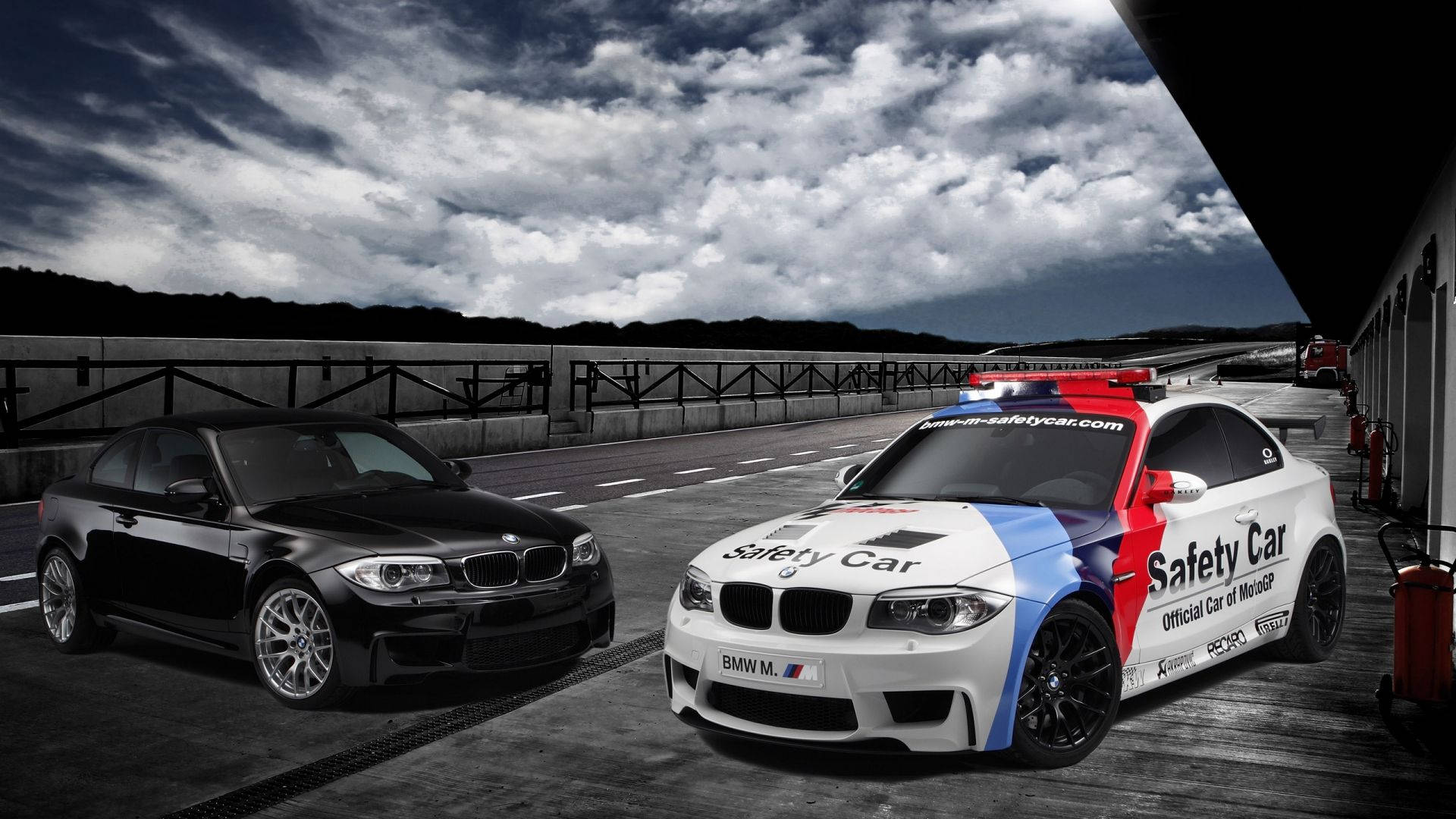 m 桌布 壁紙 — 兩輛BMW賽車，一黑一白的安全車帶有紅藍條紋，停在賽道上，背景是戲劇性的暴風雲。