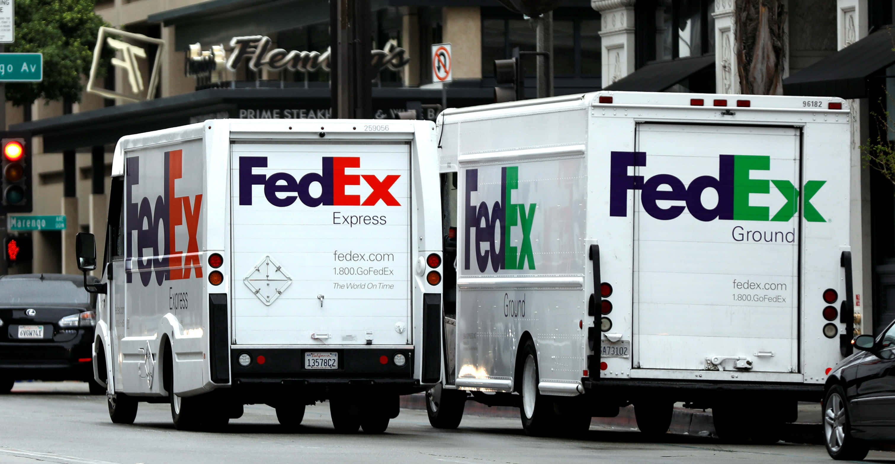 聯邦快遞 桌布 壁紙 — 兩輛FedEx送貨卡車並排停放在城市街道上，背景有商店門面和交通號誌。
