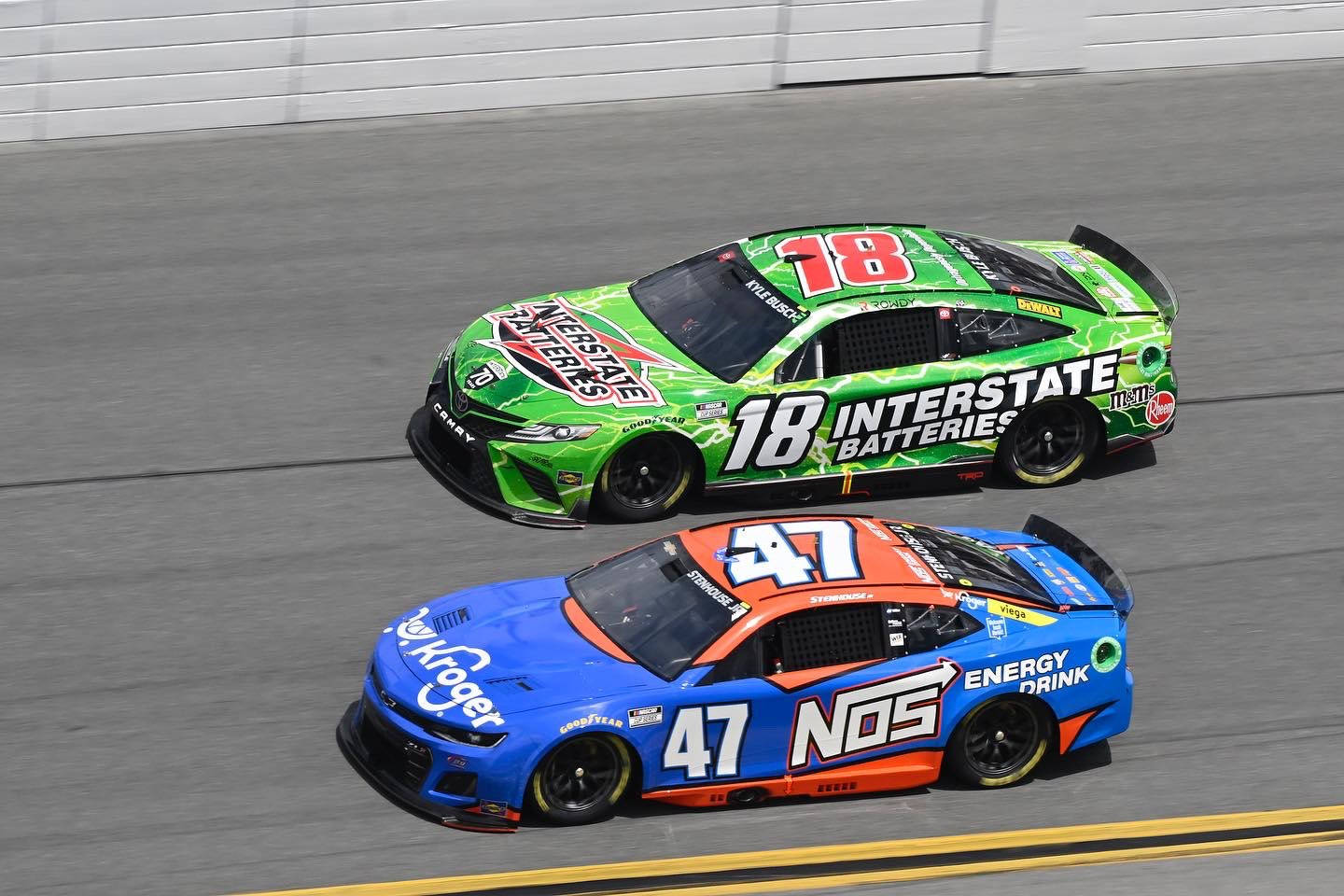 Racing 桌布 壁紙 — 兩輛NASCAR賽車，一輛綠色車身號碼18，一輛藍橙色車身號碼47，在賽道上並排飛馳。