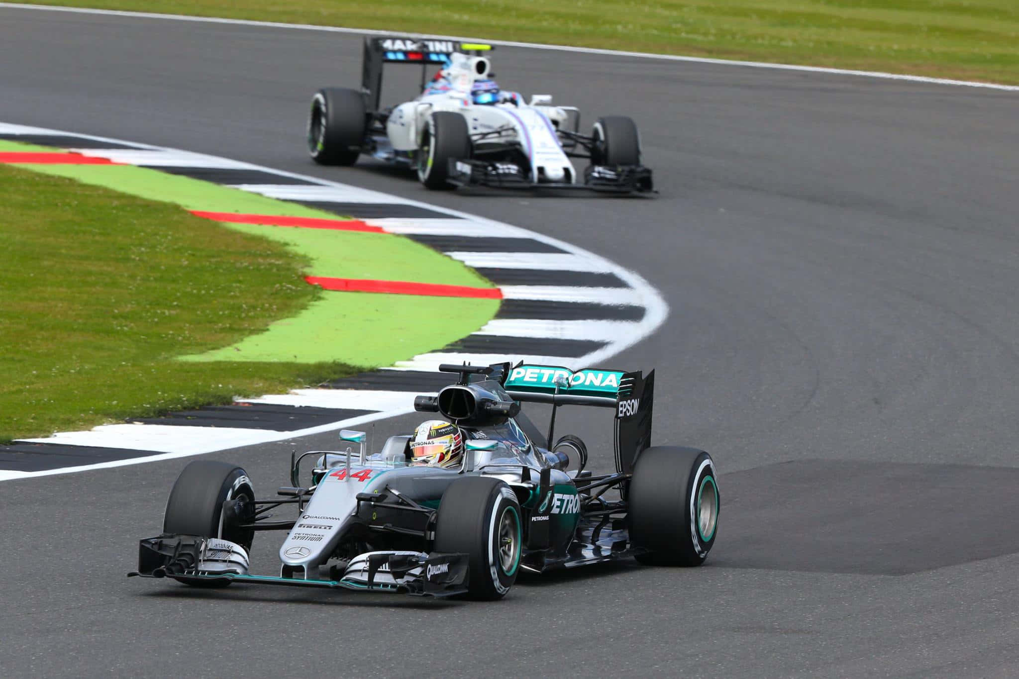 HD F1 2016 桌布 壁紙 — 兩輛一級方程式賽車在潮濕的賽道上緊密競賽，可見綠色草地和格子狀路緣。