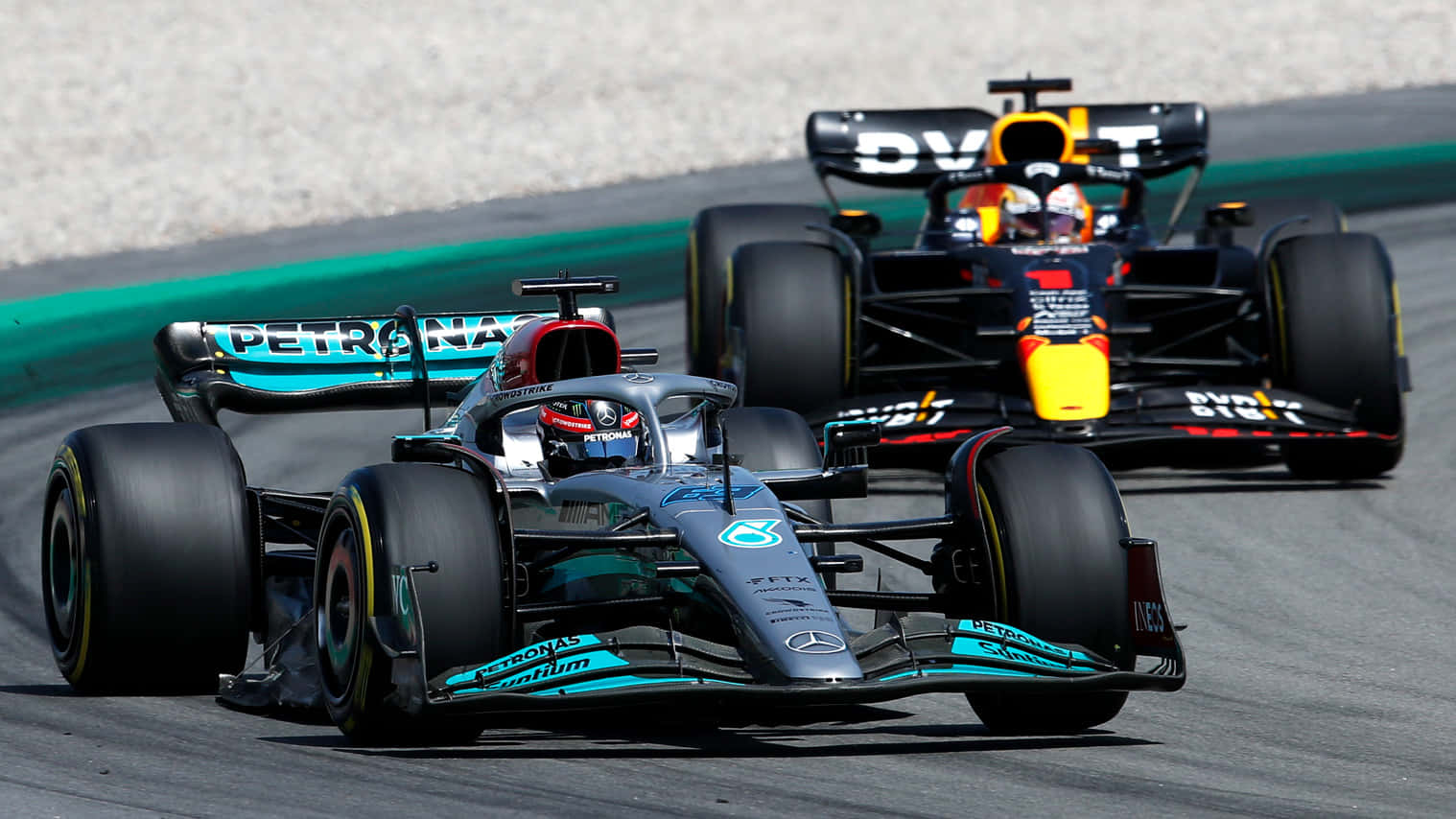Formula One 桌布 壁紙 — 兩輛一級方程式賽車在陽光明媚的賽道上並肩競速，賽道設有碎石緩衝區和綠色路緣石。