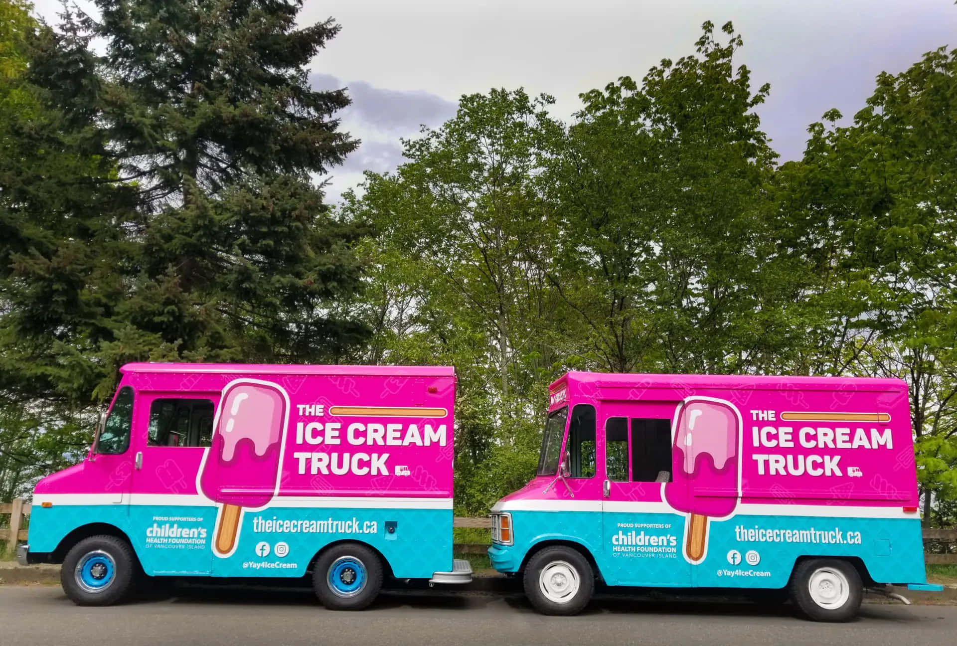 Ice Cream Truck 桌布 壁紙 — 兩輛亮粉色和藍綠色的冰淇淋車並排停放在陰天天空下，後面有綠樹。