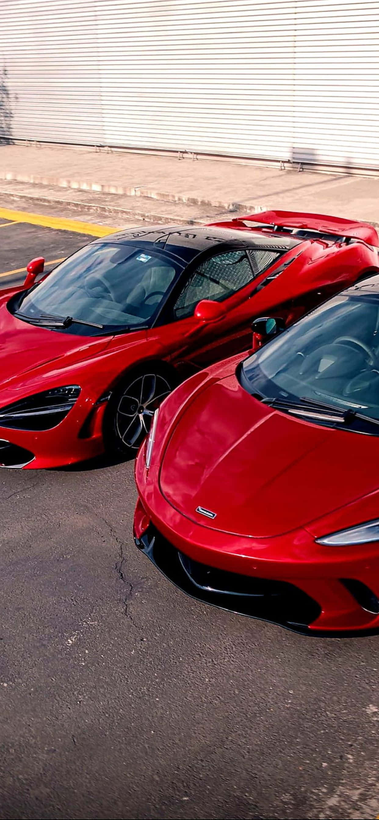 紅色動圖 桌布 壁紙 — 兩輛亮面紅色McLaren超級跑車並排停放在瀝青路面上，旁邊是波紋金屬牆。