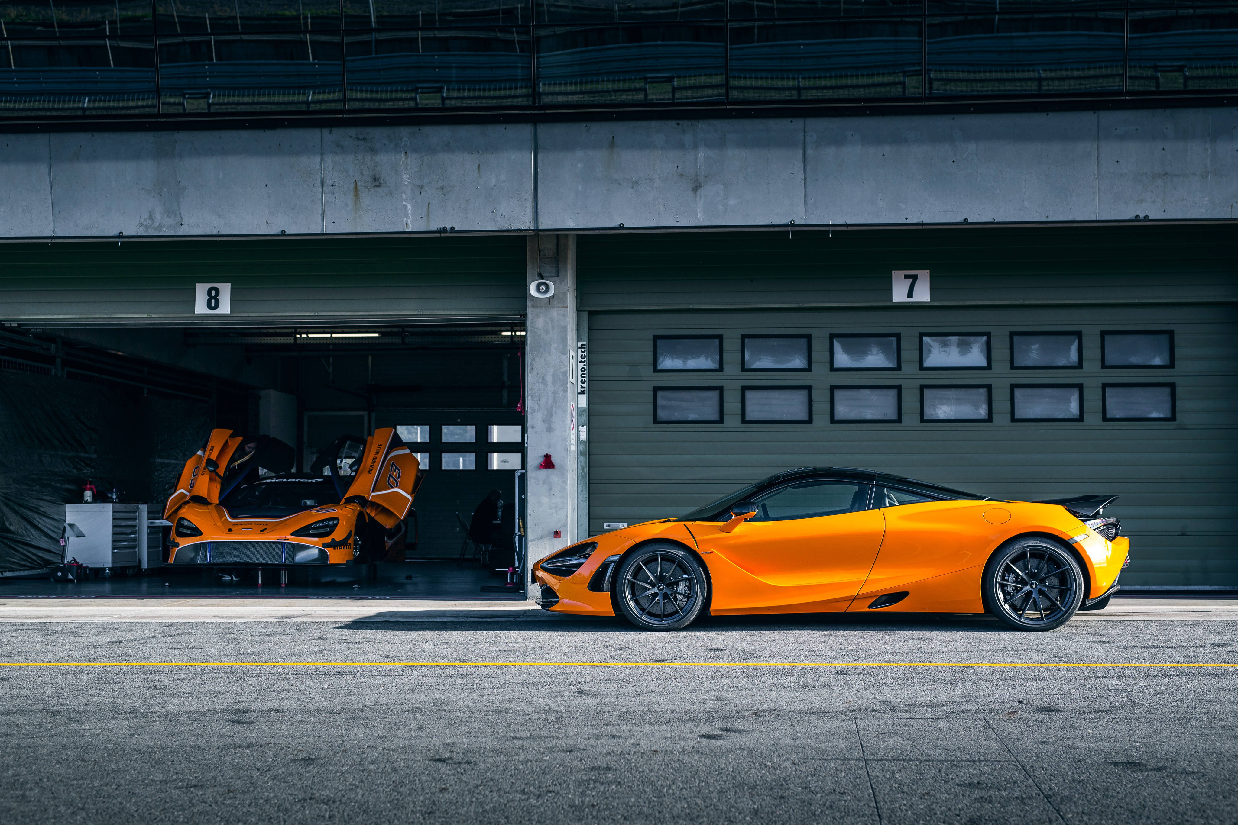 Mclaren 720s 桌布 壁紙 — 兩輛充滿活力的橙色McLaren超級跑車停在混凝土車庫中，其中一扇車門打開，露出內部。