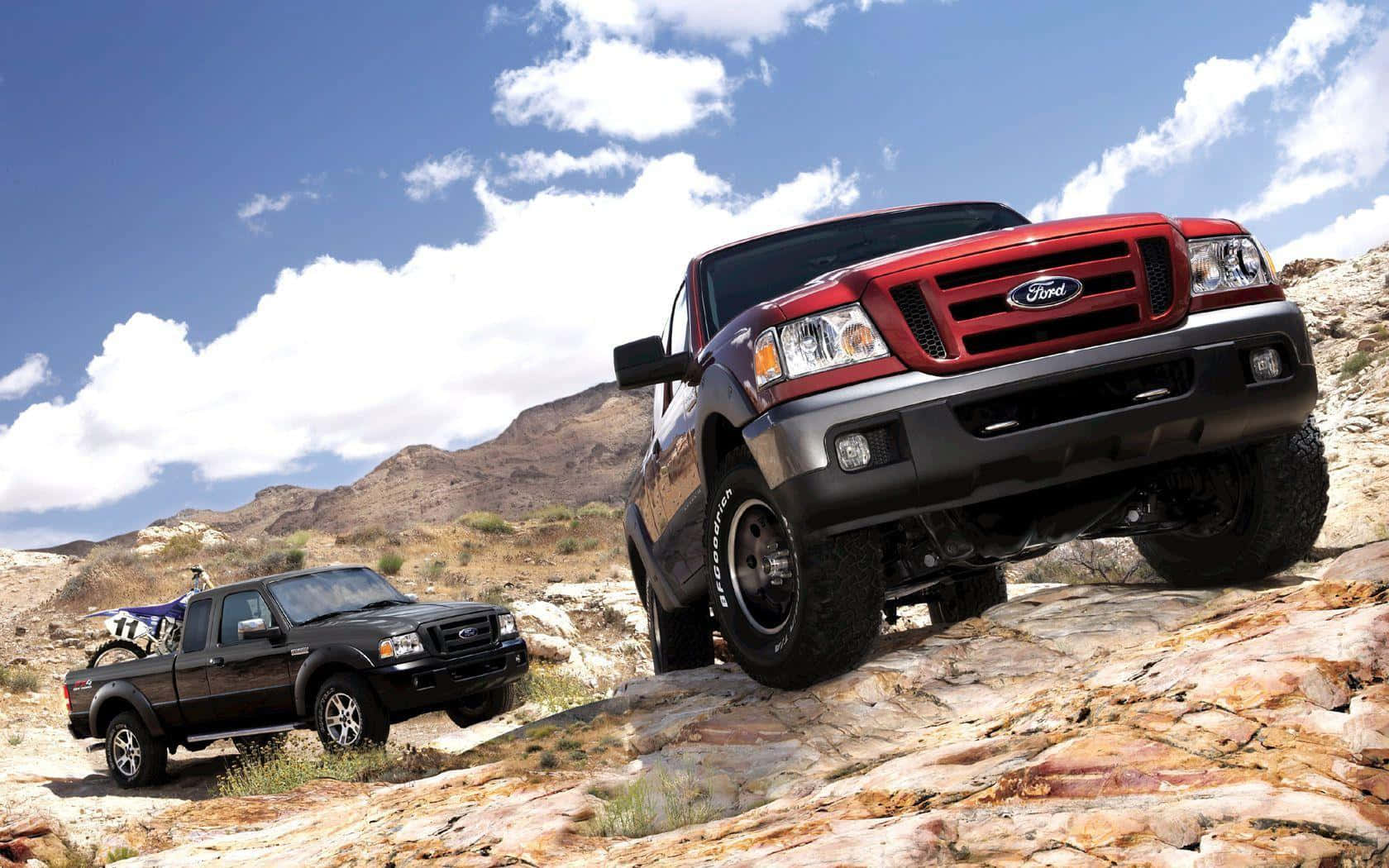 Ford Ranger 桌布 壁紙 — 兩輛堅固的福特卡車在明亮的藍天和蓬鬆的白雲下征服岩石地形。