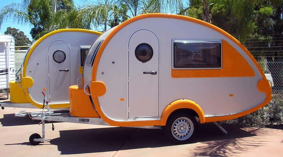 Caravan 桌布 壁紙 — 兩輛帶有白色和橙色裝飾的復古水滴形拖車在陽光明媚的日子裡停放在棕櫚樹下。