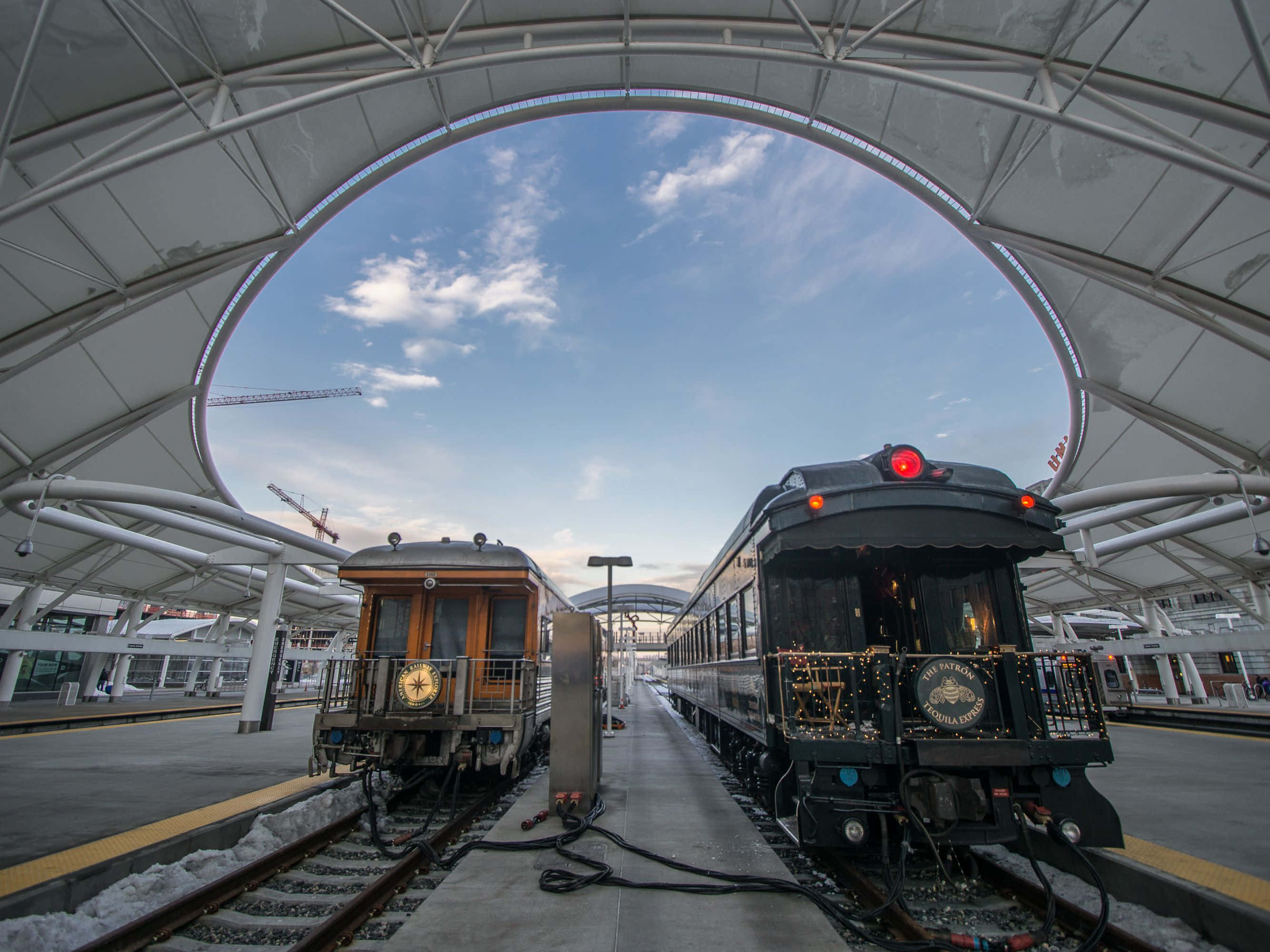 Train Station 桌布 壁紙 — 兩輛復古火車在現代拱形車站屋頂下相對，地面有雪，上方是藍天。