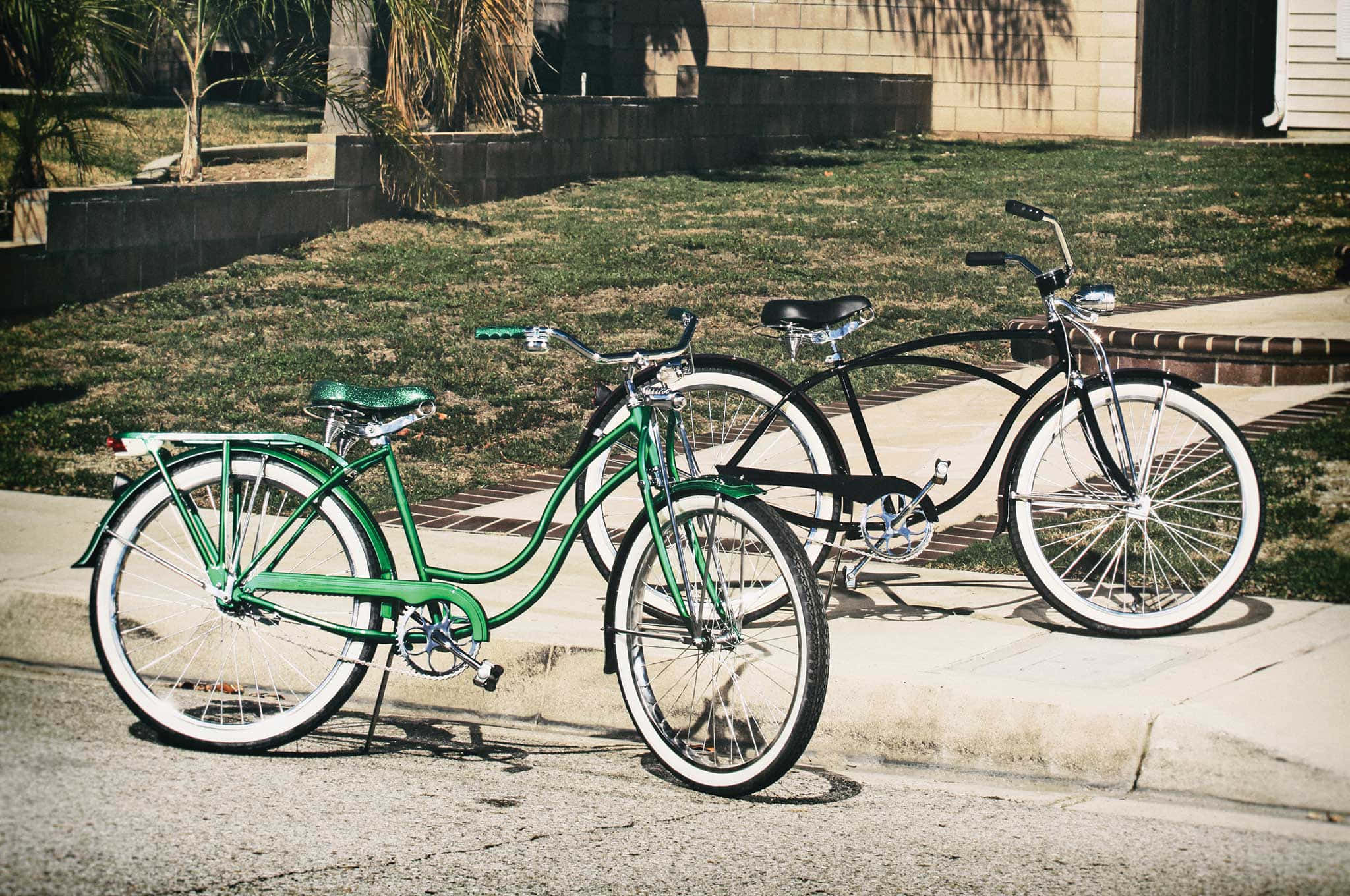 Beach Cruiser 桌布 壁紙 — 兩輛復古腳踏車，一綠一黑，停放在陽光普照下草地旁的人行道上。