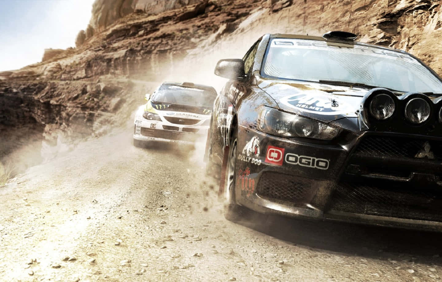 1440p Dirt Showdown 桌布 壁紙 — 兩輛拉力賽車在塵土飛揚的山路上激烈競速，在明亮的日光下揚起滾滾塵土。
