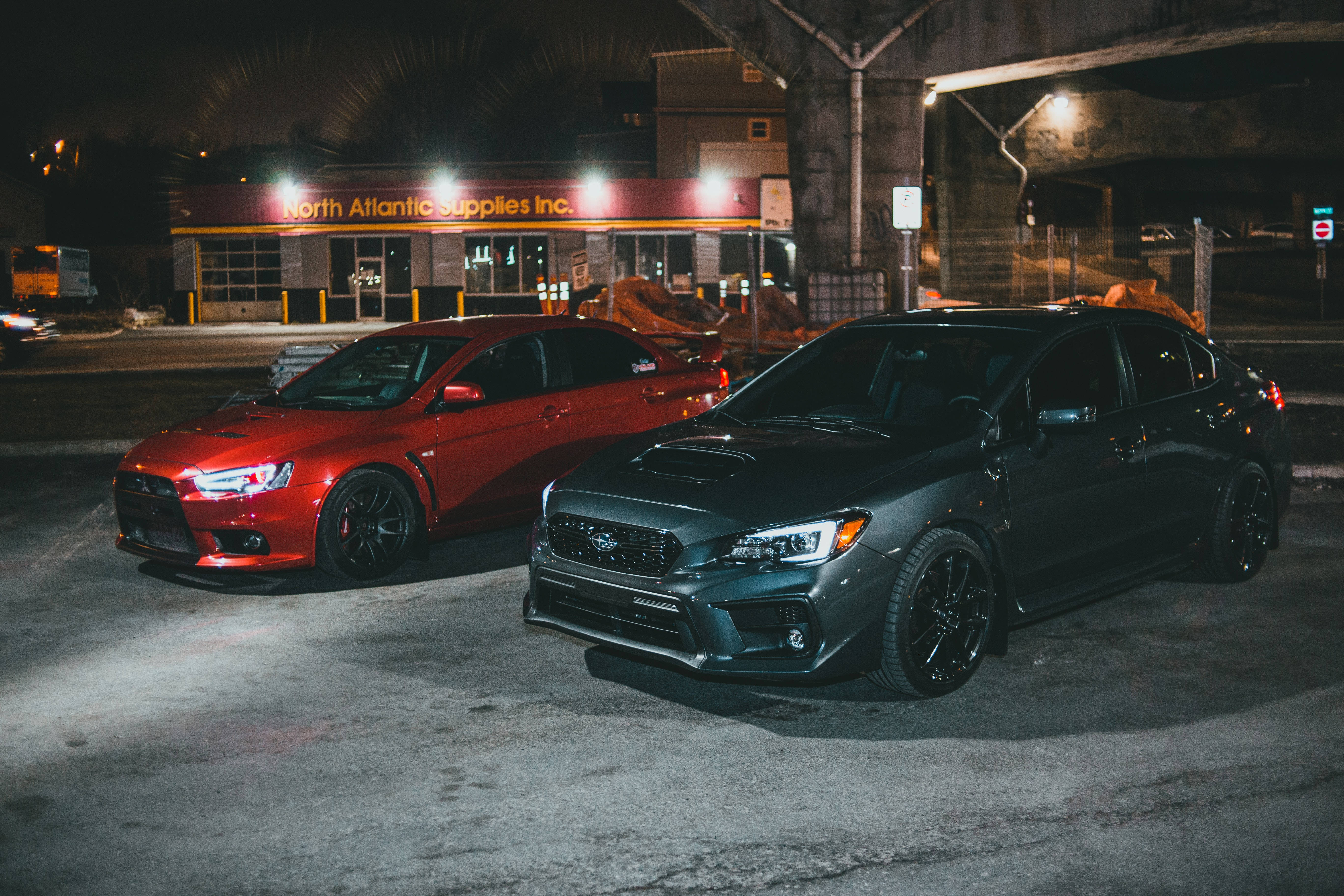 4K 桌布 壁紙 — 兩輛改裝的Subaru轎車在夜間停放在橋下，發光的車頭燈和城市街燈在潮濕的路面上投射出倒影。