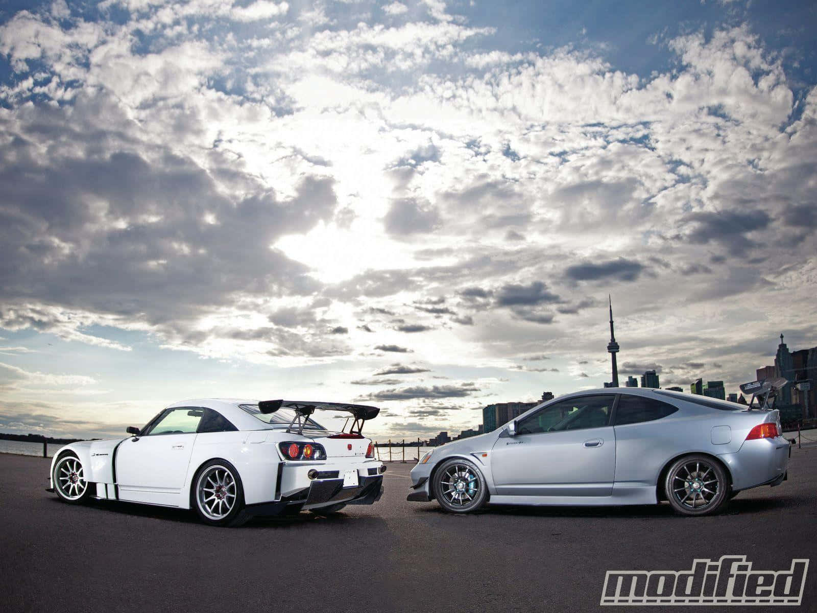 Rsx Type-s 桌布 壁紙 — 兩輛改裝跑車停在海濱，背景是陰天和城市天際線。