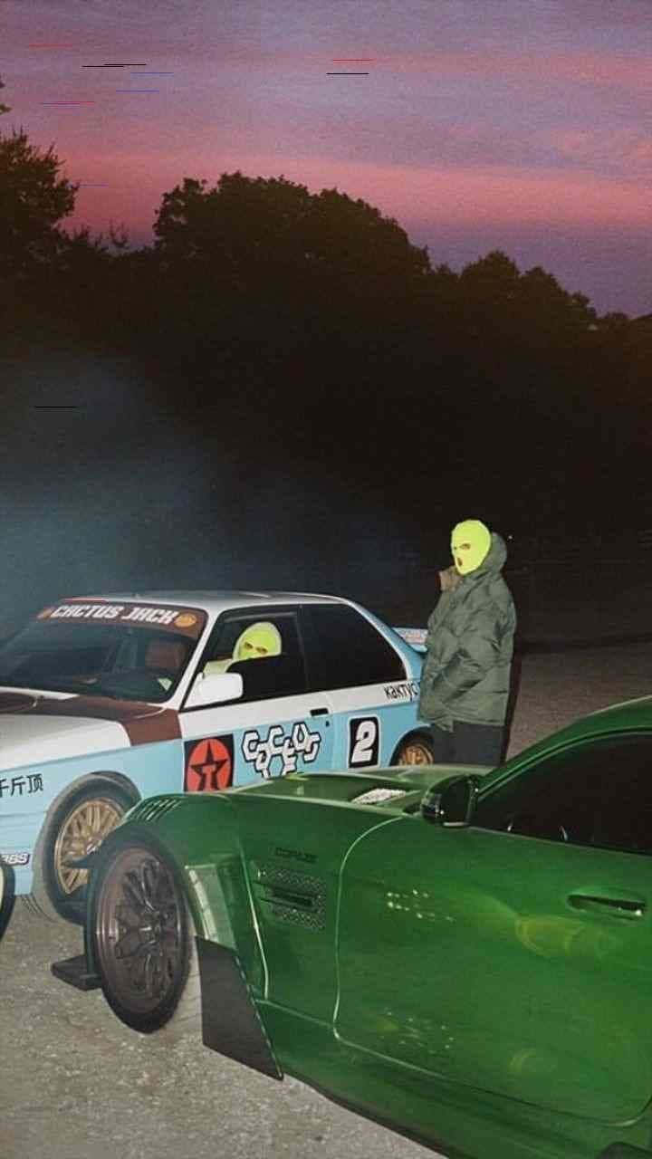 美學 桌布 壁紙 — 兩輛改裝車在黃昏時停泊，發光的綠色蒙面人物站在它們旁邊，天空呈現粉紫色。