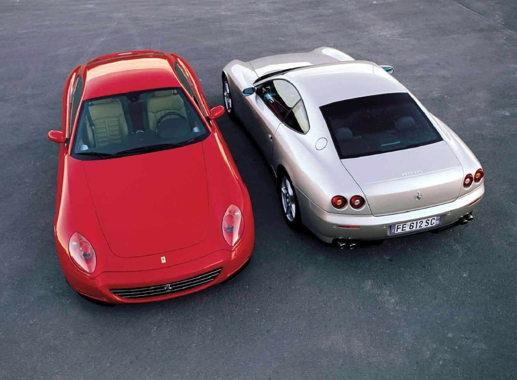 Ferrari 612 Scaglietti 桌布 壁紙 — 兩輛時尚法拉利，一輛鮮紅色和一輛金屬銀色，並排停放在灰色瀝青路面上。