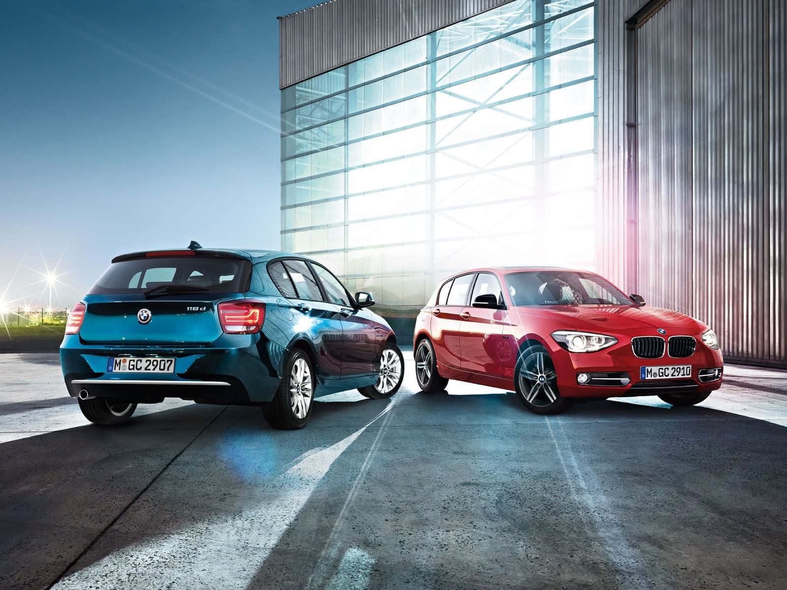 Bmw 1 Series 桌布 壁紙 — 兩輛時尚的BMW，一藍一紅，停在現代玻璃和金屬建築前，在明亮的日光下。