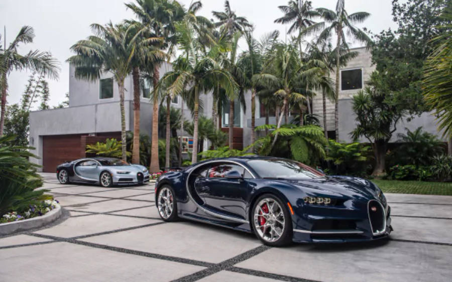 4K 桌布 壁紙 — 兩輛時尚的Bugatti超級跑車停放在瓷磚車道上，周圍環繞著棕櫚樹和現代豪宅。