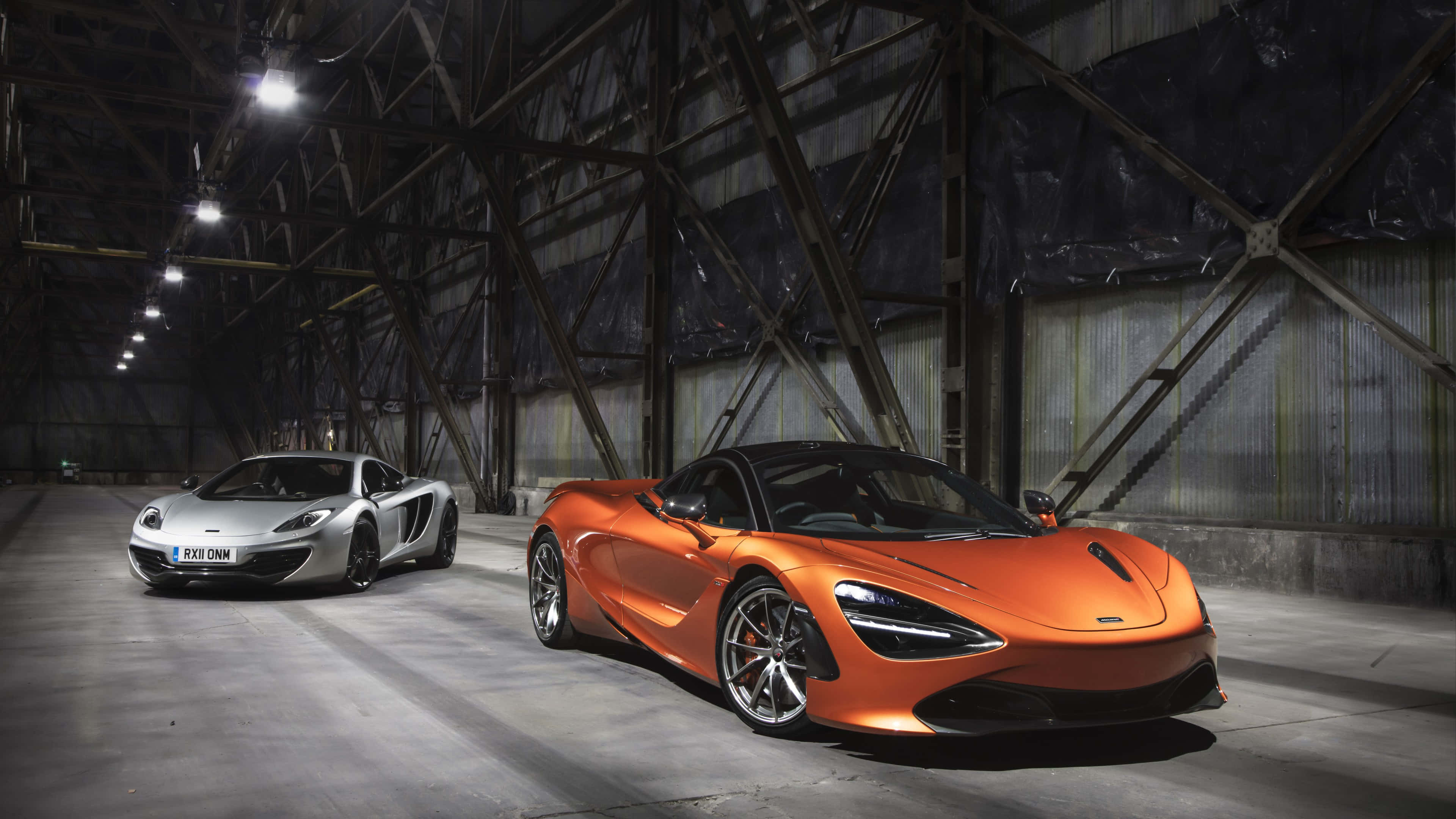 4K Mclaren 720s 桌布 壁紙 — 兩輛時尚的McLaren超級跑車，銀色和橙色，在廣闊倉庫內的工業燈光下閃耀。