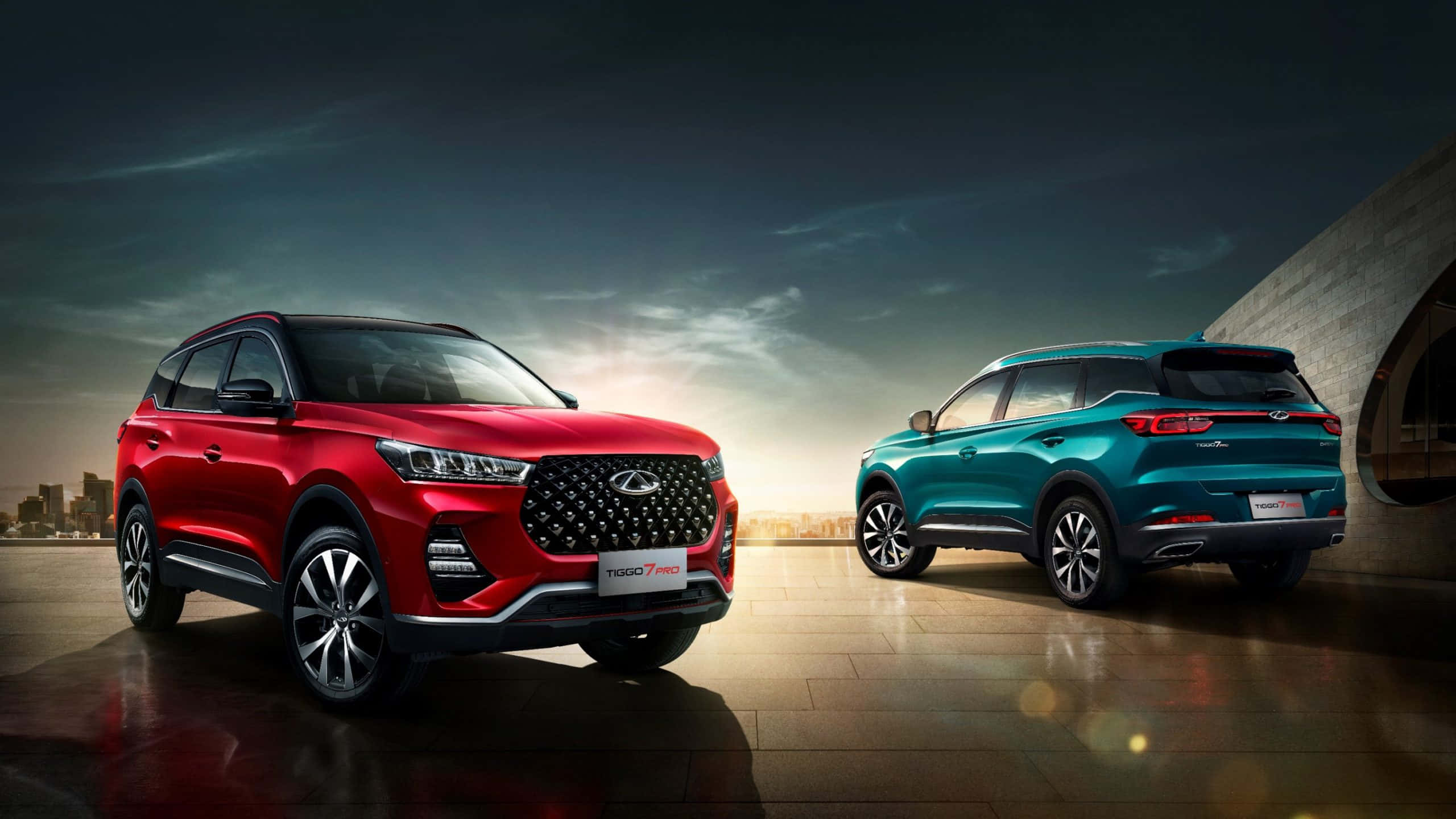 Chery 桌布 壁紙 — 兩輛時尚的SUV（紅色和藍綠色）在戲劇性的暮色天空和城市天際線背景下相對而立。