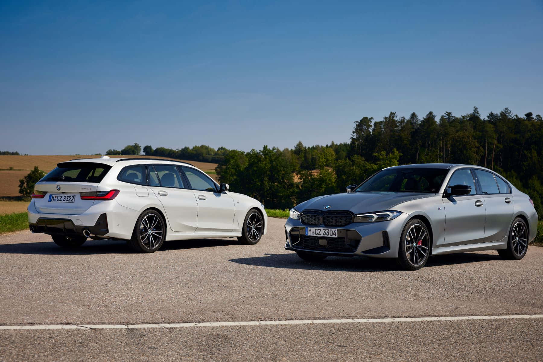Bmw 3 Series 桌布 壁紙 — 兩輛時尚的寶馬汽車（銀色和白色）停泊在鄉村道路上，背景是晴朗的藍天和樹木。