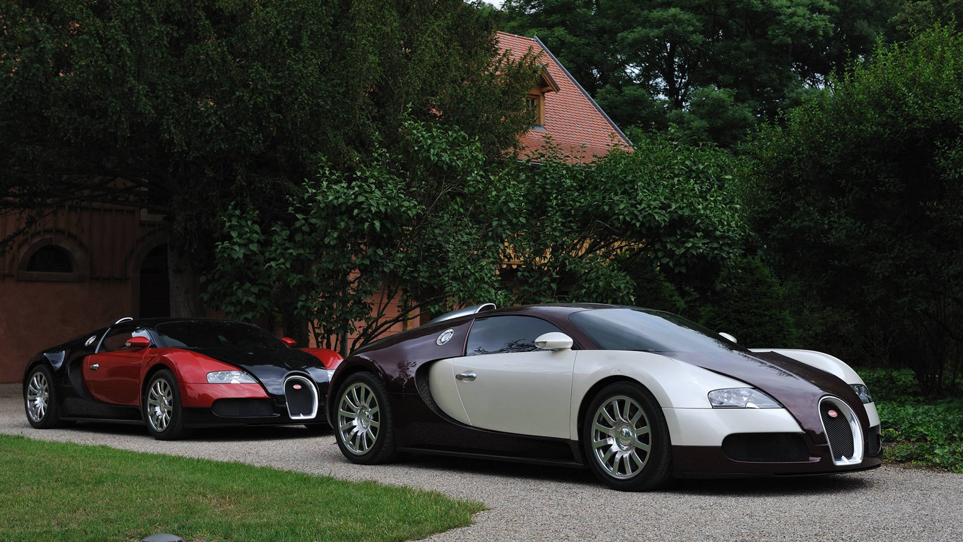 Cool Bugatti 桌布 壁紙 — 兩輛時尚的布加迪超級跑車停在碎石車道上，旁邊是鬱鬱蔥蔥的綠色草坪和一棟磚房。