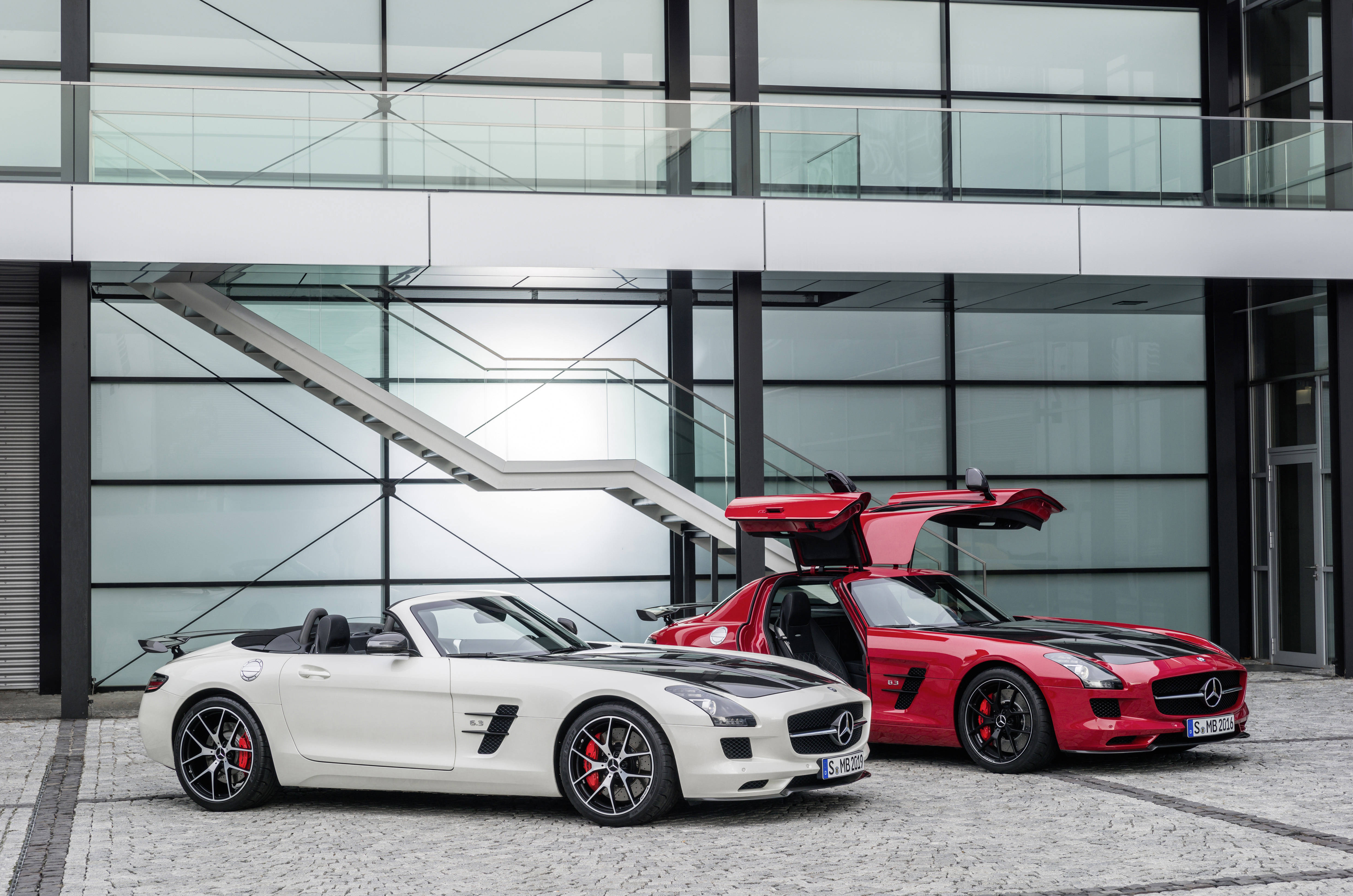 Luxury 桌布 壁紙 — 兩輛時尚的梅賽德斯 SLS 跑車，白色和紅色，停在現代玻璃建築前，鷗翼車門敞開。